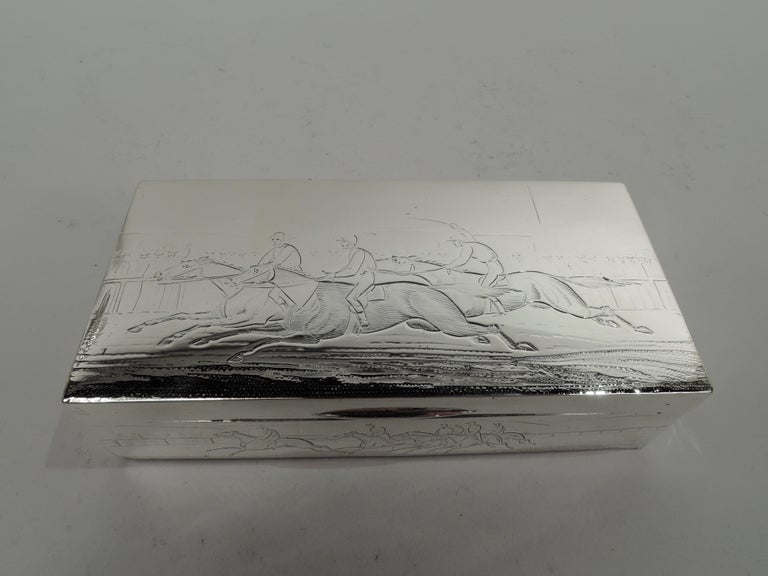 Victorian sterling silver box. Made by William Thomas Wright & Frederick Davis in London in 1885. Rectangular with straight sides. Cover flat and hinged with tapering tab. Engraved racecourse scenes. On cover and front horses thunder past spectators