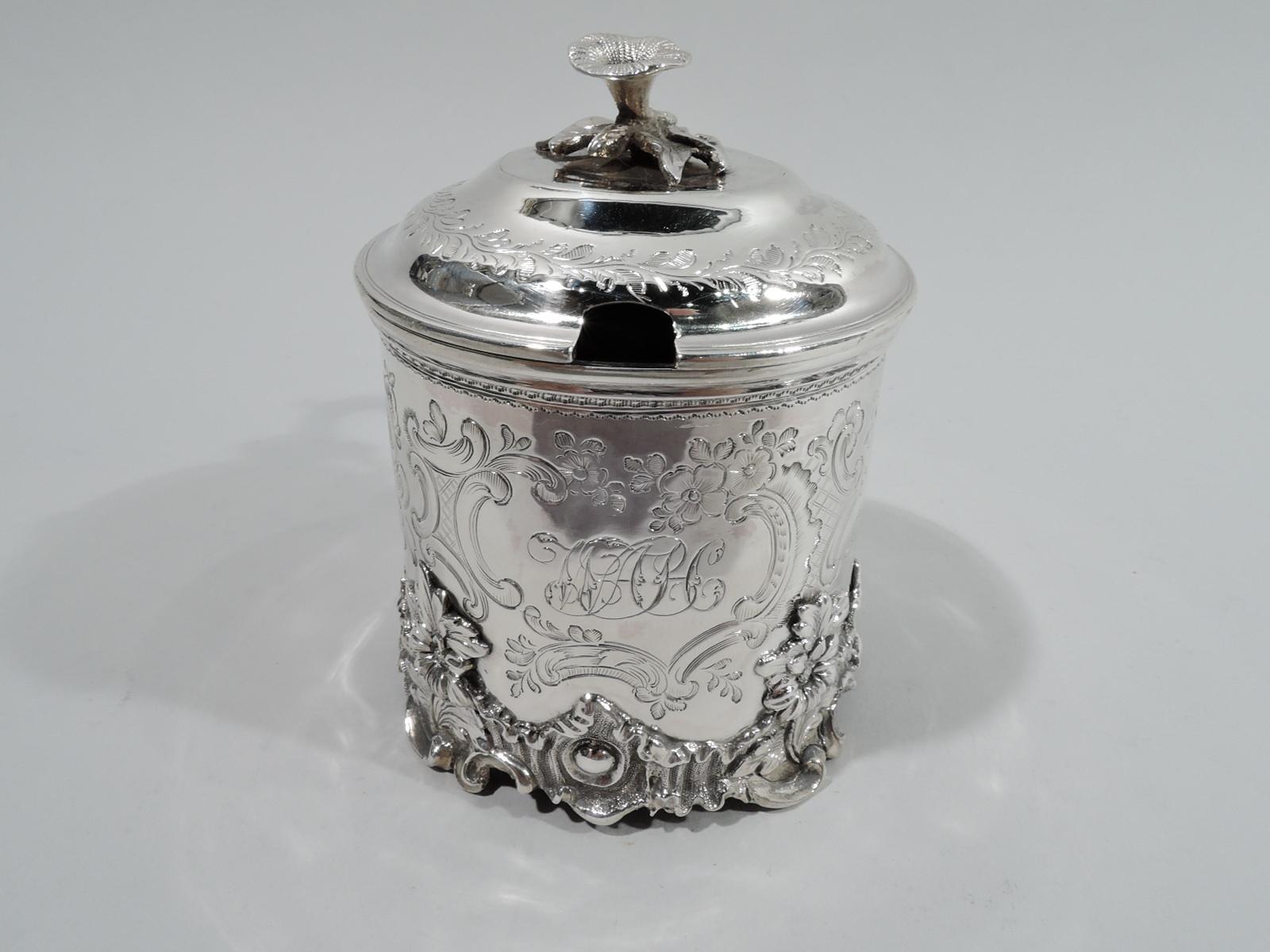 Victorian sterling silver mustard pot. Made by Edward Edwards in London in 1845. Drum-form with applied scroll and flower border at base. Cover hinged and domed with flower finial and capped s-scroll handle. Engraved flowers, leaves, and scrolls.