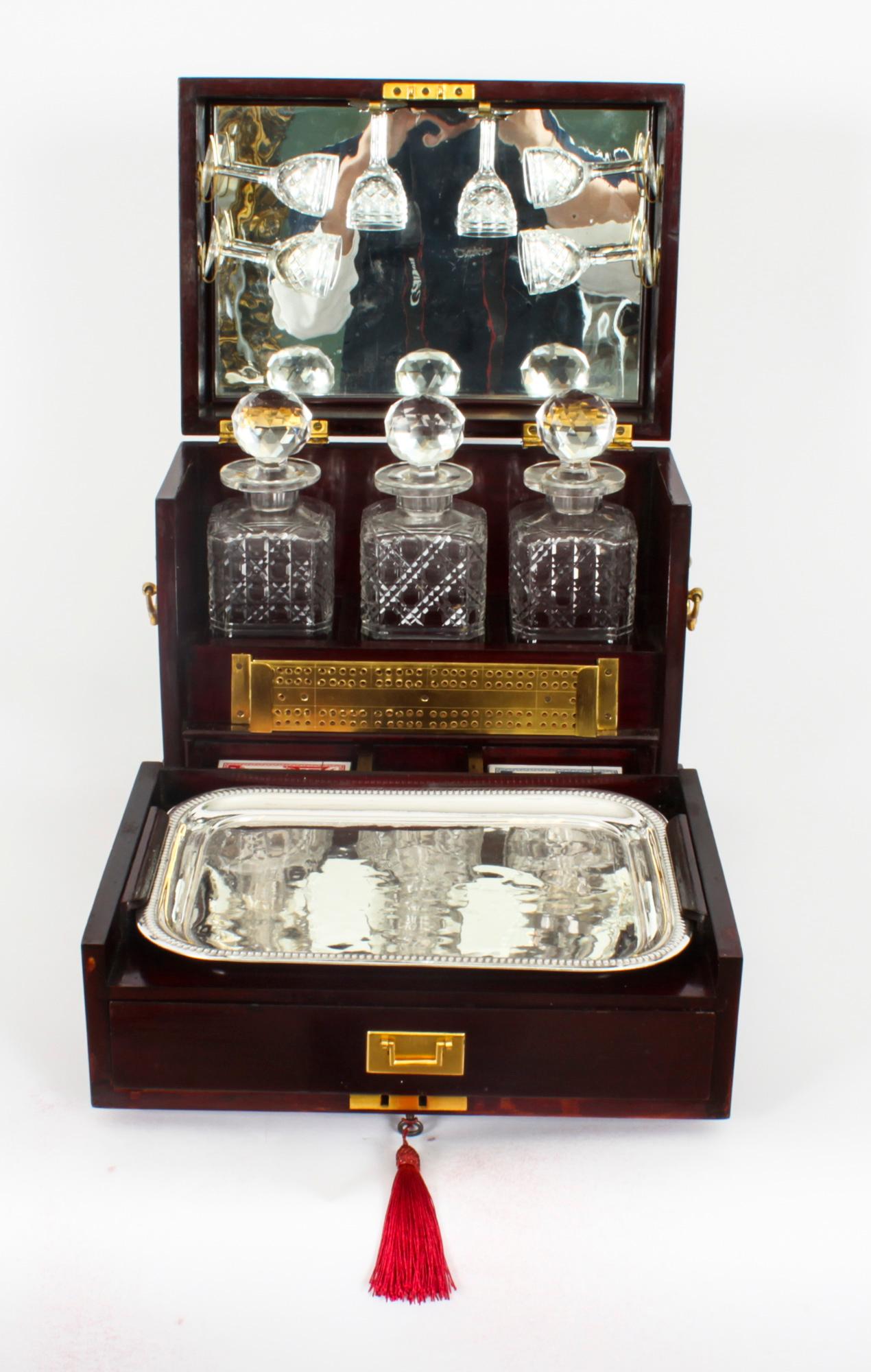 This is a fabulous antique English tantalus, circa 1880 in age. It consists of three cut crystal liquor bottles with stoppers, 6 etched stemmed glasses, a silver plated tray and a fitted cribbage board - all housed in a magnificent mahogany casket