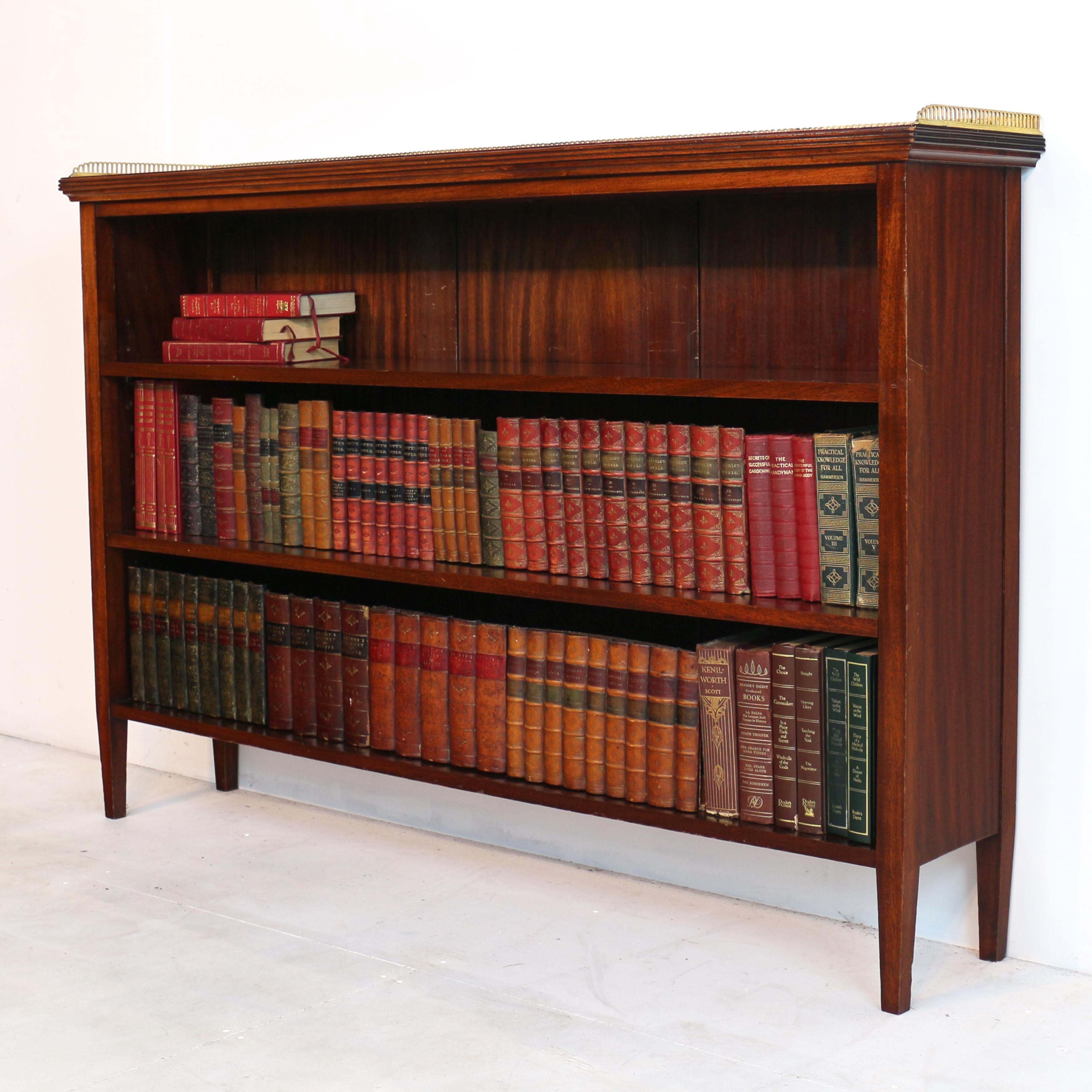 An antique English late Victorian walnut open bookcase bookcase in the Regency style, very nice quality and unusual in that the top has a pierced brass three quarter-gallery and reeded edge, the open front with two adjustable shelves and raised on