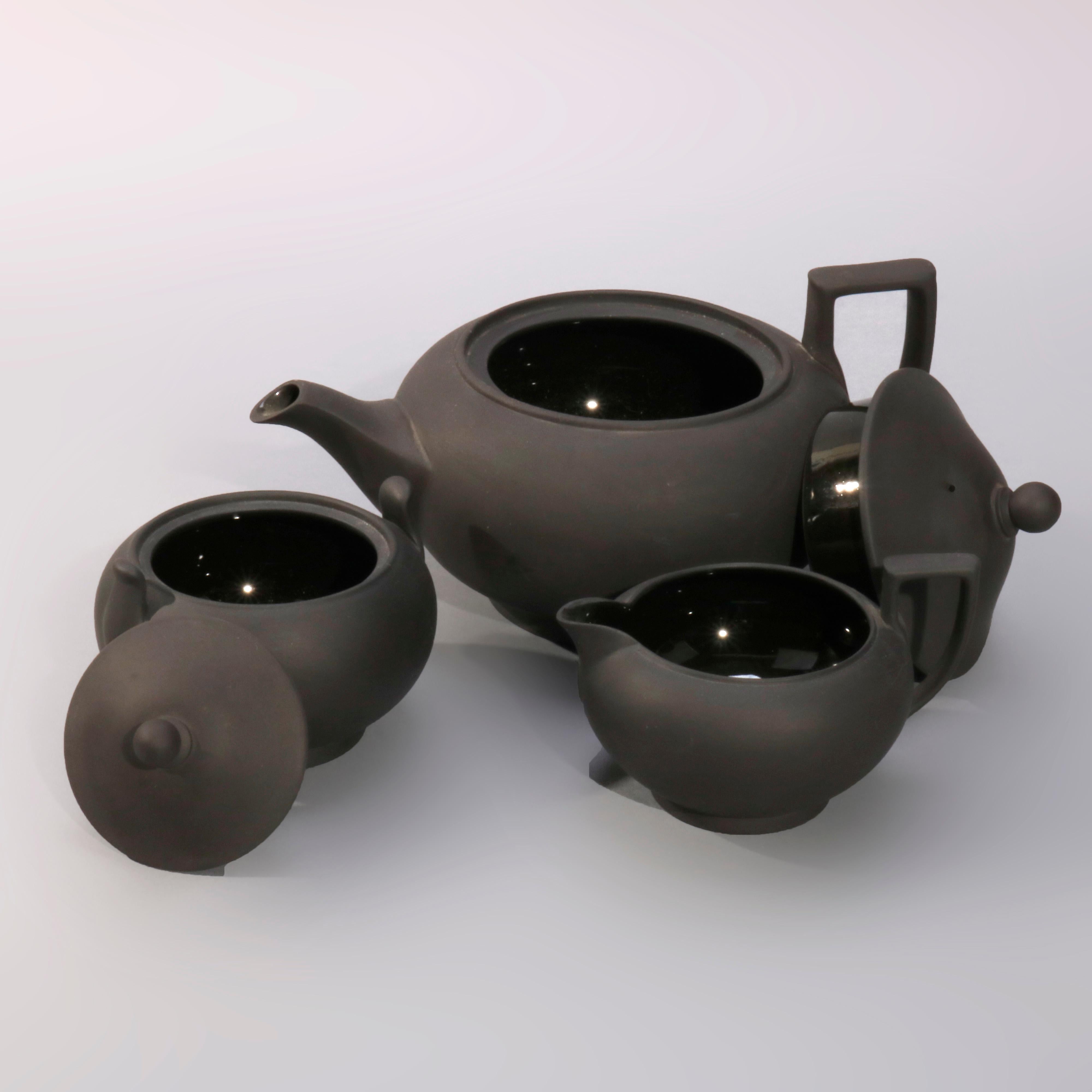 An antique English black basalt stoneware 3-piece teapot set by Wedgwood offers matte exteriors with glazed interiors and includes footed teapot, lidded sugar and creamer, two items stamped Wedgwood on base as photographed, 19th century

Measures-