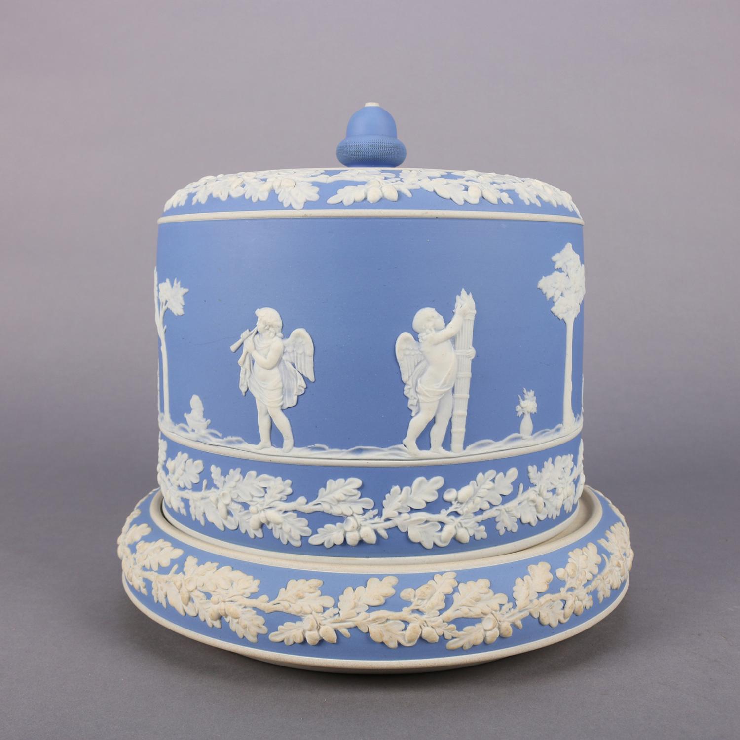 Antique English Wedgwood Jasperware porcelain cheese keeper in blue features unglazed stoneware encircled by classical base-relief scenes and oak leaf garland, includes cheese plate with cylindrical dome with acorn finial, 19th century

Measures: