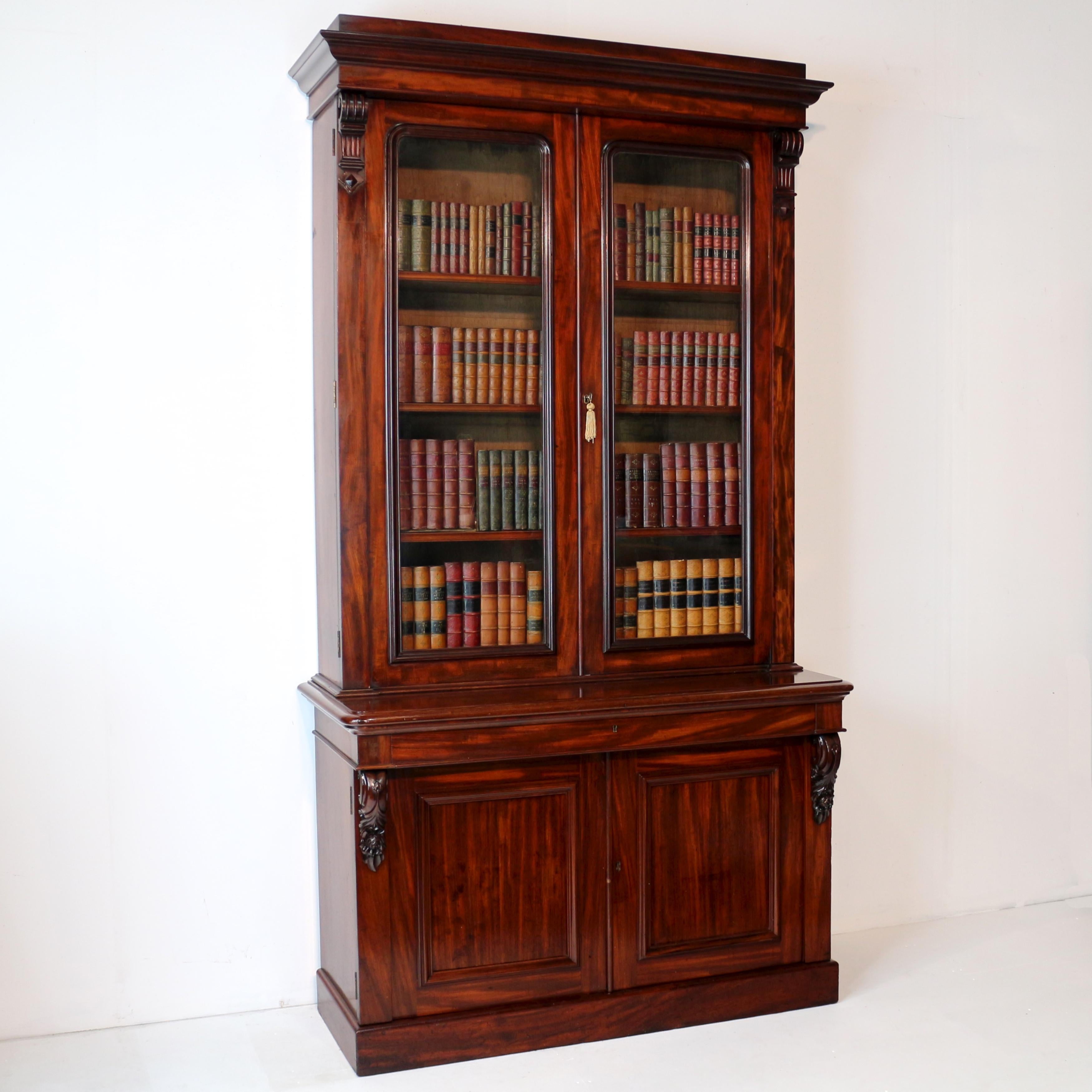 Una estantería/armario de dos puertas de caoba cubana Guillermo IV de gran calidad que data de c.1830. Con una cornisa moldurada escalonada sobre dos puertas acristaladas que encierran estantes ajustables, la base con una encimera moldurada sobre un