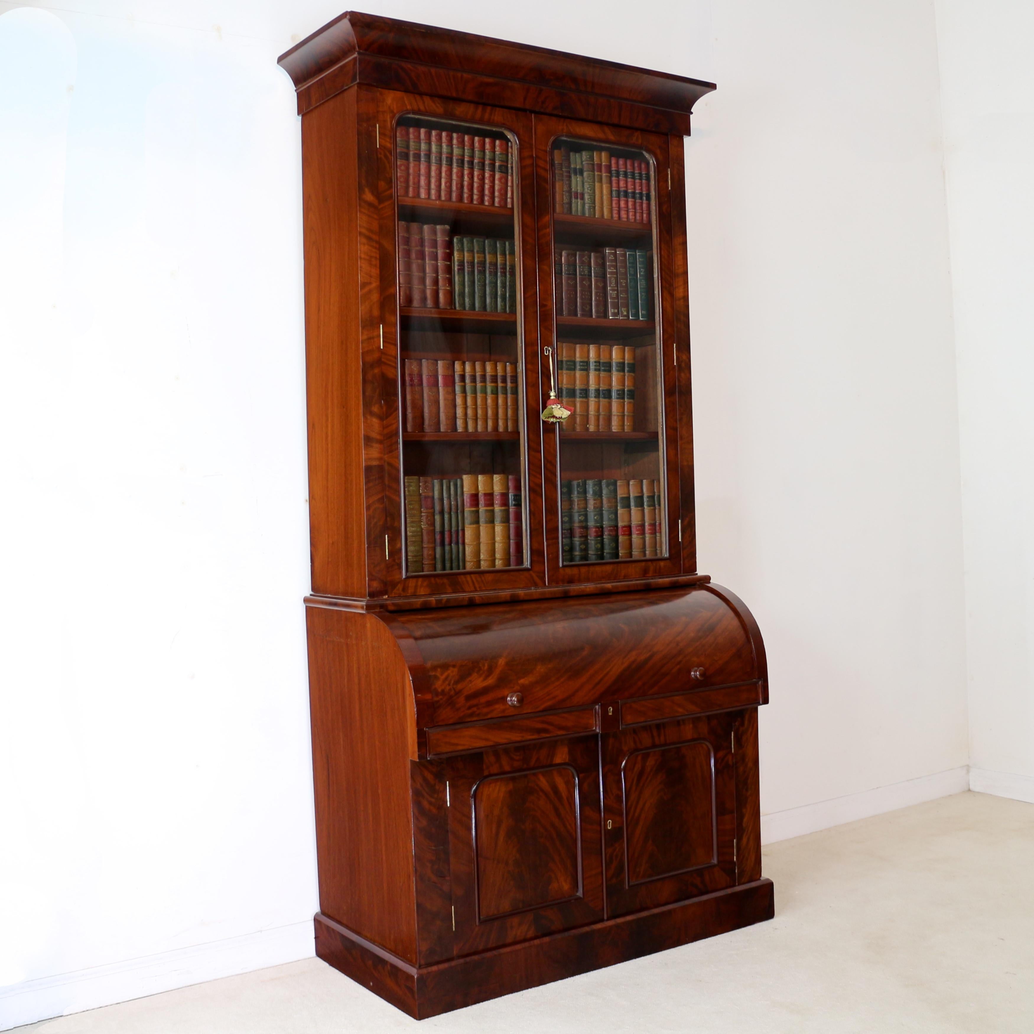 A super William IV/early Victorian cylinder bookcase in beautifully figured flame mahogany, with a rectangular moulded cornice above two glazed doors enclosing adjustable shelves, the projecting base with a revolving cylinder door concealing a