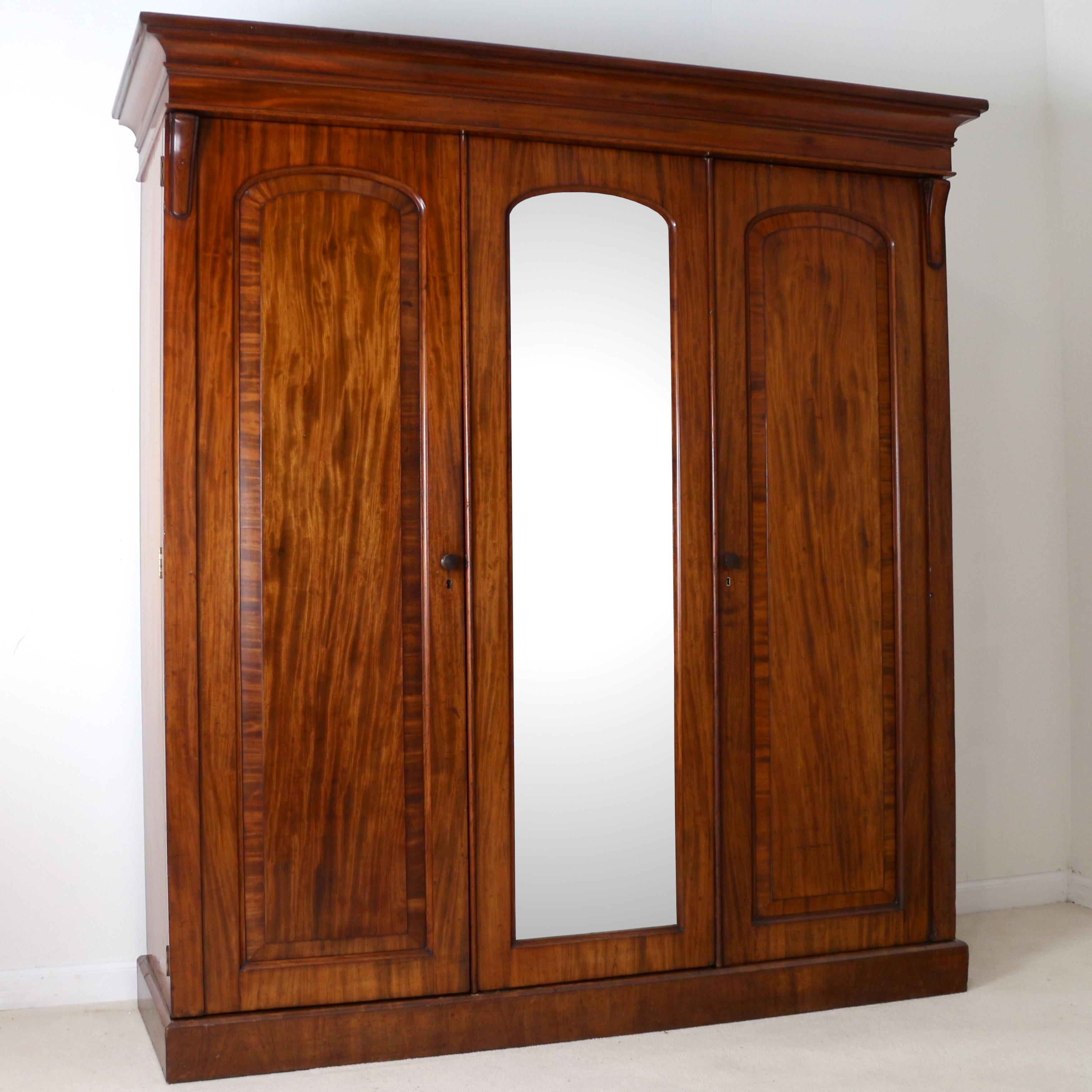 A good quality English William IV mahogany three door wardrobe dating, circa1830. With a moulded cornice above three arched crossbanded panelled doors which open to reveal a fitted interior with a full length hanging space, sliding trays and