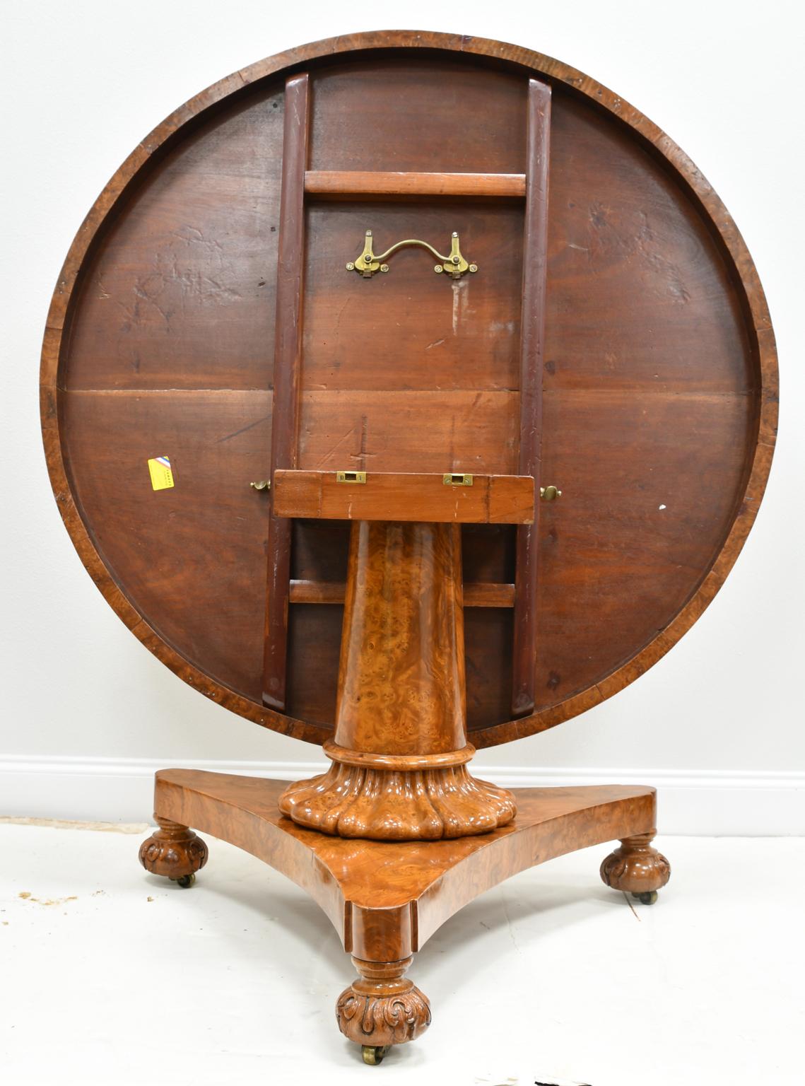 A fine William IV center table or loo table in beautiful burl ash wood with round top and apron on cylindrical column over a tripartite (triform) base with concave sides resting on carved bun feet. Burl wood top features a captivating pattern that
