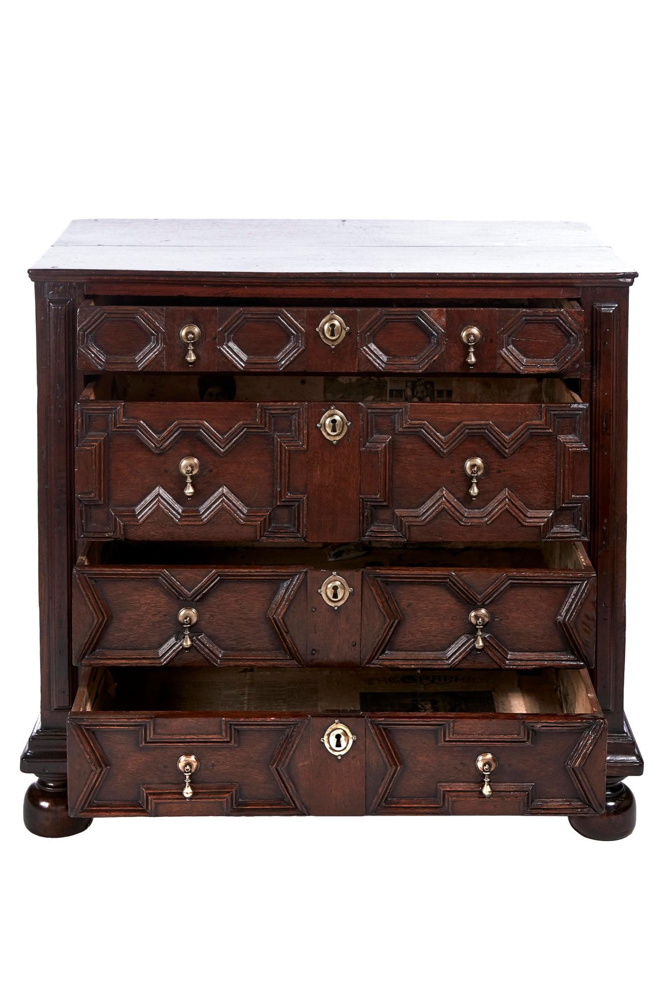 Antique English William & Mary Jacobean oak paneled geometric chest of drawers having a lovely oak top, paneled sides, 4 long drawers with geometrical moldings. Lovely antique newspaper lined drawers, standing on original bun feet.
Lovely color and
