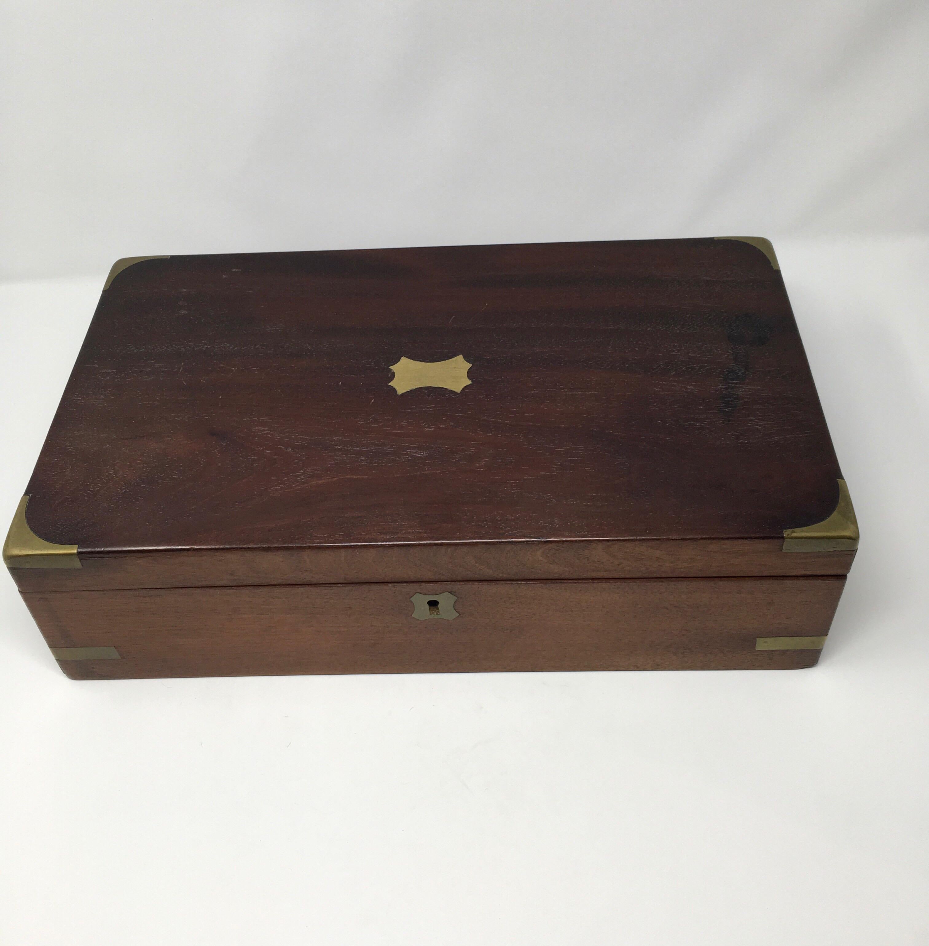 This is a lovely antique English writing box. The wood box features a brass plate on the top which is usually inscribed with the owners name or initials. The top corners are wrapped in brass and brass inserts decorate four points of the bottom