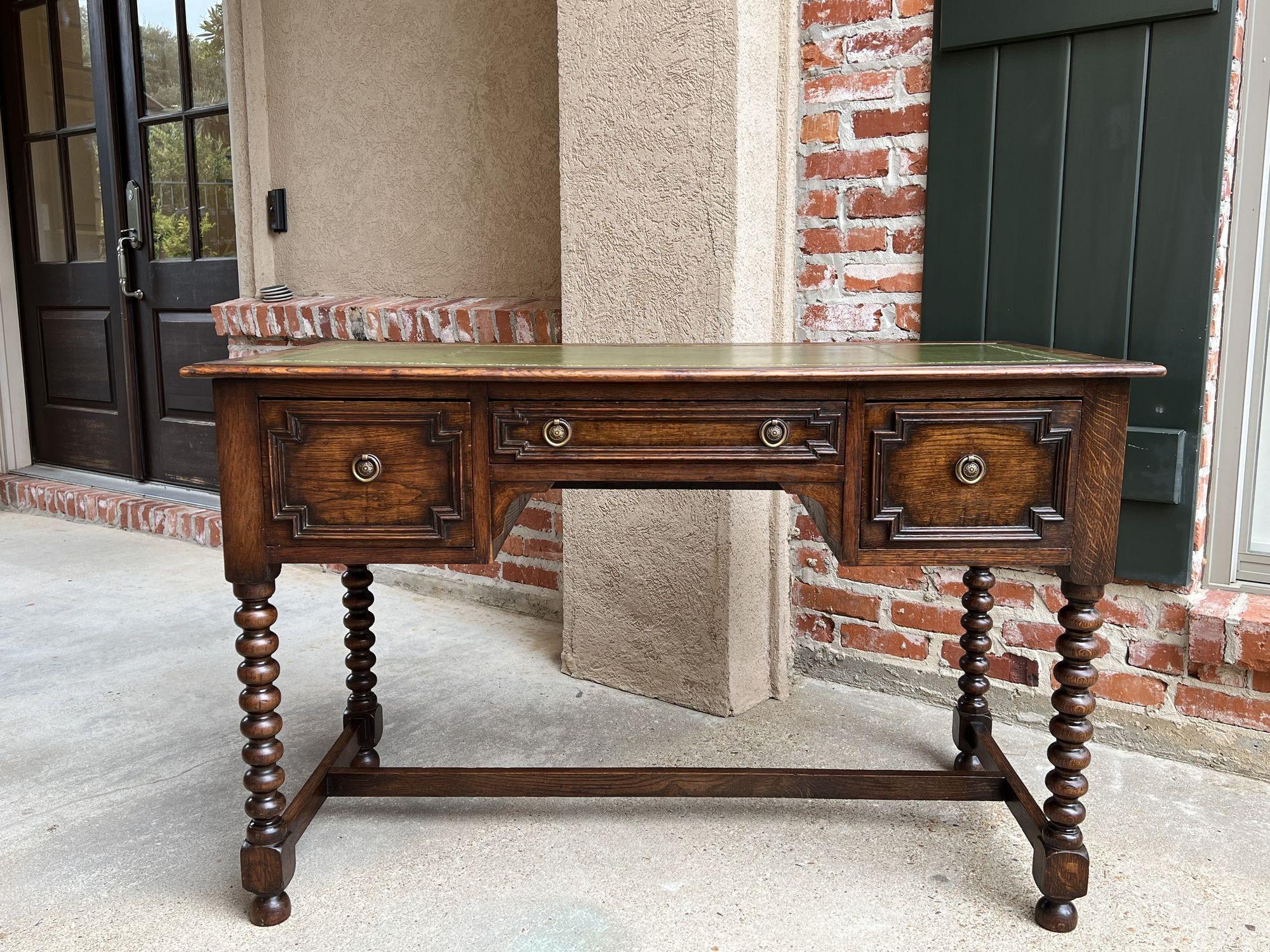 Antique English writing desk table Jacobean carved oak green leather w bobbin legs.

Direct from England, a beautiful antique writing desk in lovely Jacobean style! 
Long center drawer is flanked by wide drawers to either side; all three have