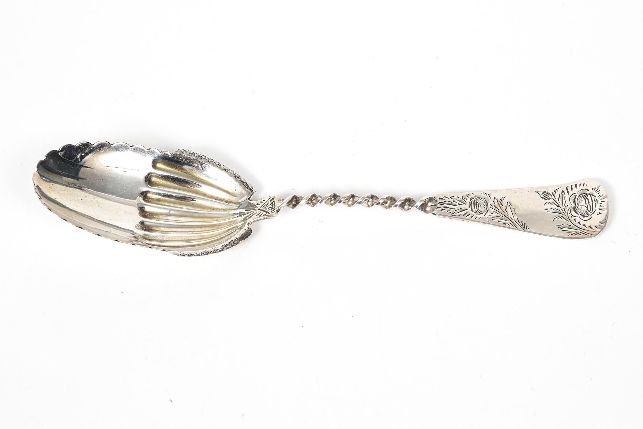 Ornate sterling silver serving spoon featuring an engraved floral handle that is twisted where it meats the bowl.. The spoon area is an oval with ridges inside and a scalloped edge. Marked sterling on the back.