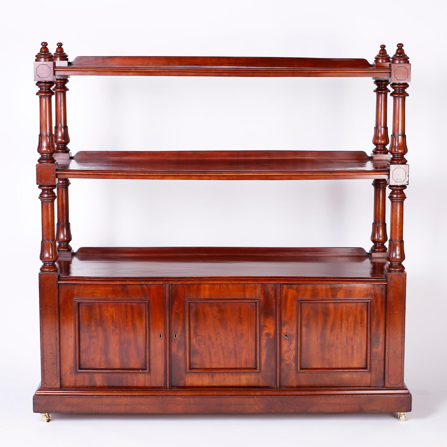 William IV English étagère or server, hand crafted in well grained mahogany having two shelves with turned and carved supports with a lower cabinet featuring a zinc lined wine cellarette over a block foot lifted by brass casters.