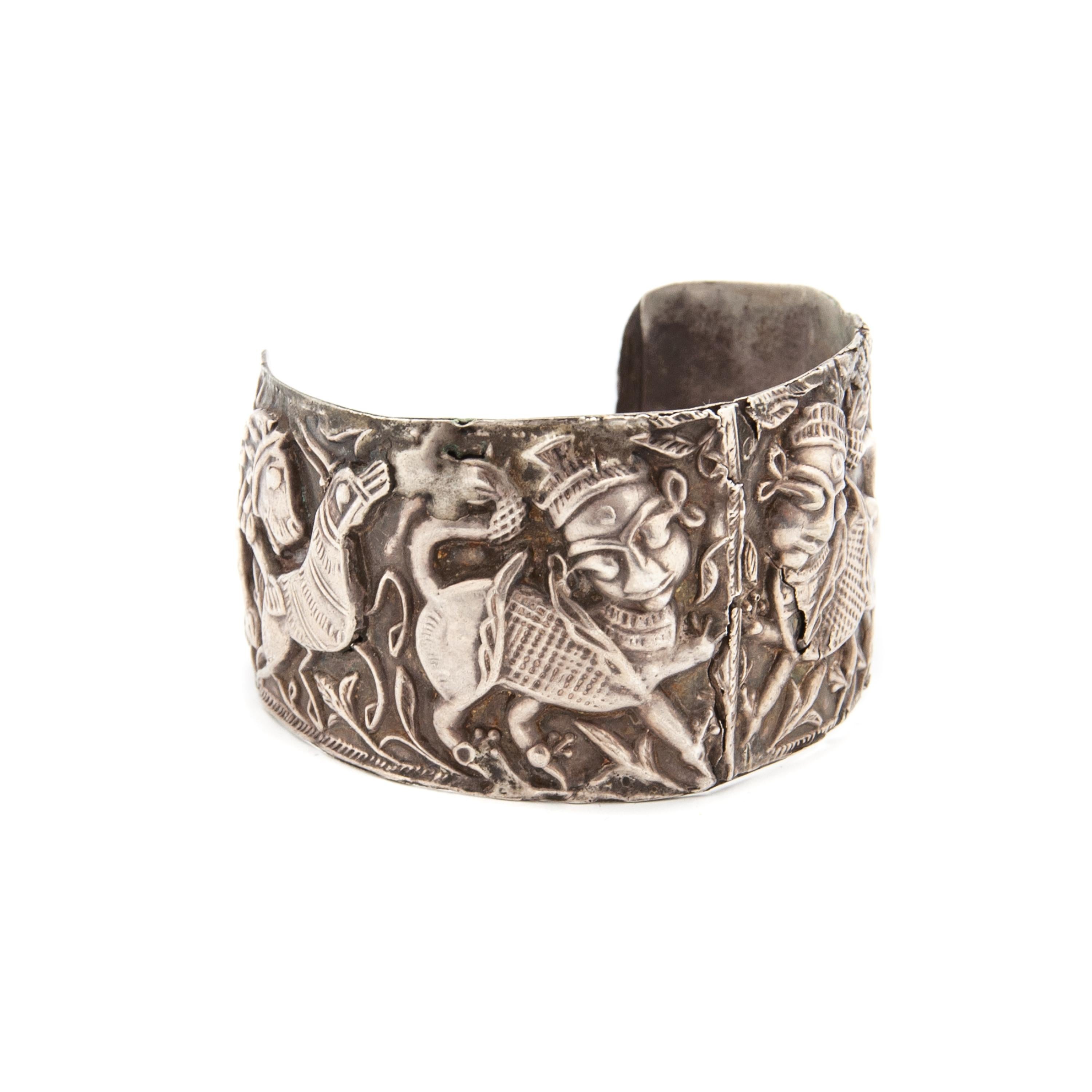 This antique silver cuff bracelet is a bold and intricately detailed piece, featuring a highly ornate repoussé (hammered relief) design depicting mythology figures and a hunting scene. The craftsmanship and artistic style suggest it originates from