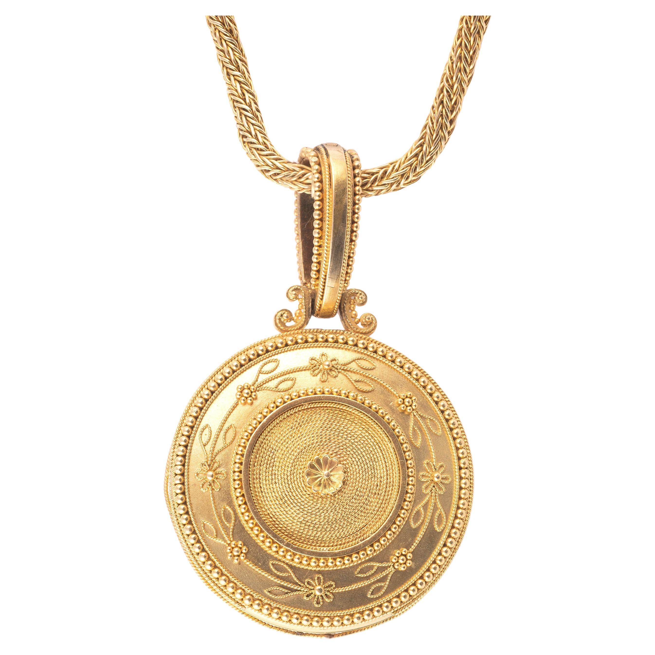 The pendant has a circular shape with a granulation and floral motif. The centre has rectangular sapphires, rose-cut diamonds and a white pearl button. Accompanied by a gold chain. Set in 18K yellow gold.

Pendant size: 3.50 x 5.60 cm.

Chain