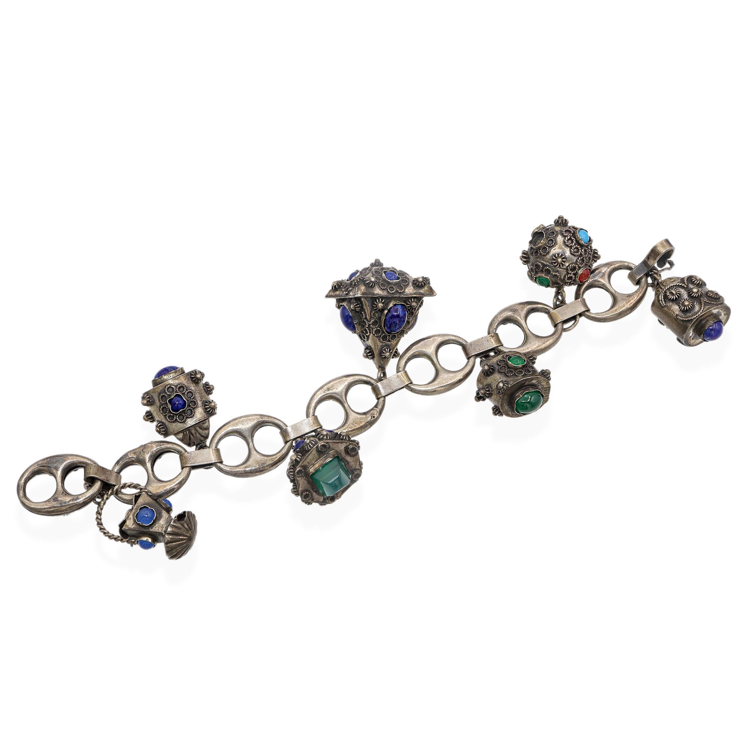 Ce remarquable bracelet ancien est un bel exemple du style néo-étrusque, caractérisé par un travail complexe de l'argent et des détails ornementaux. Réalisé avec des maillons ovales ajourés et orné de sept breloques pendantes élaborées, ce modèle