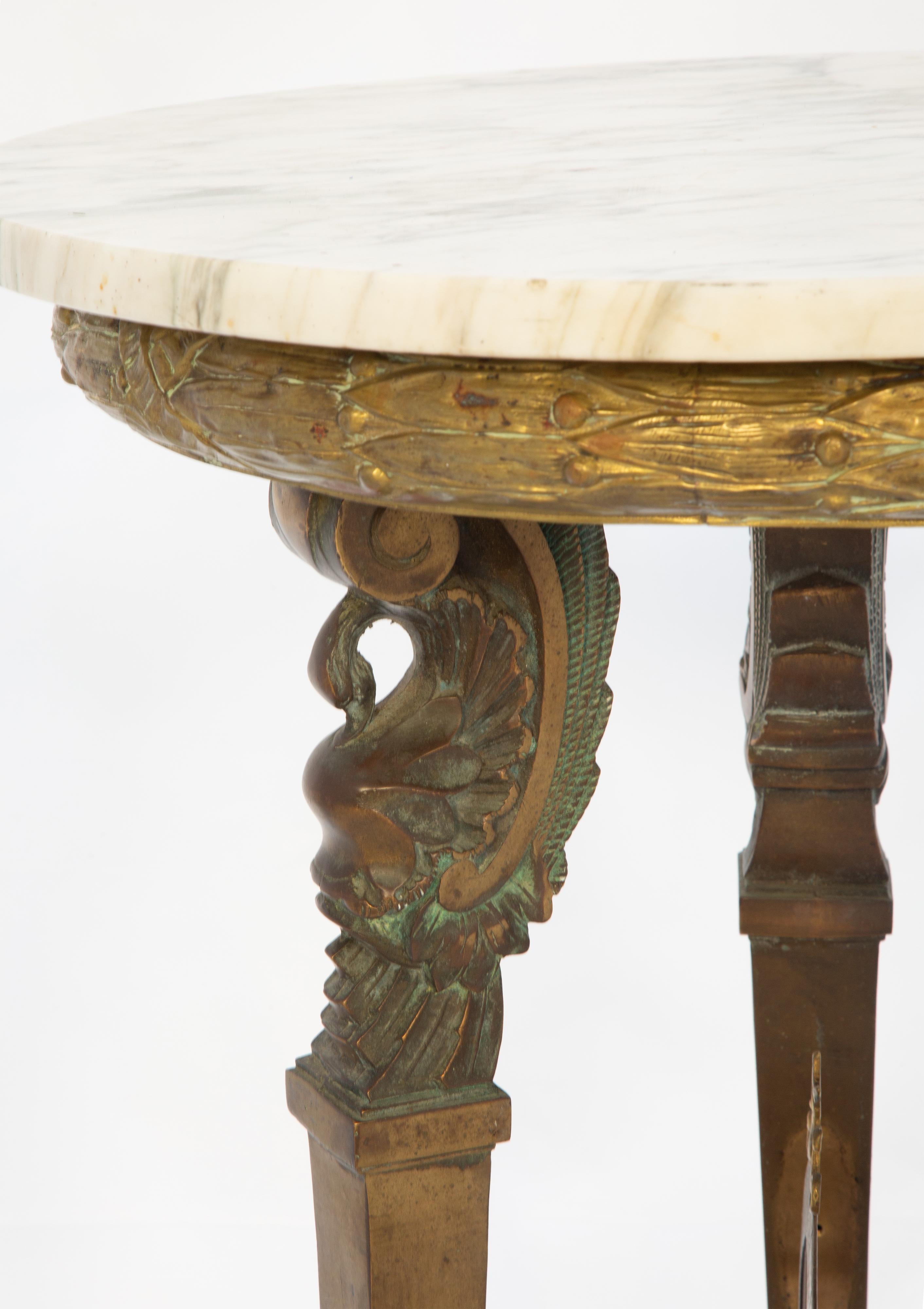 Gureidon center table having a round top of Carrara marble on an unusual base of gilt bronze in the Etruscan style. Its apron fashioned as an acanthaine wreath, raised on a trio of tapering square-section legs headed with C-scrolls and swans, ending