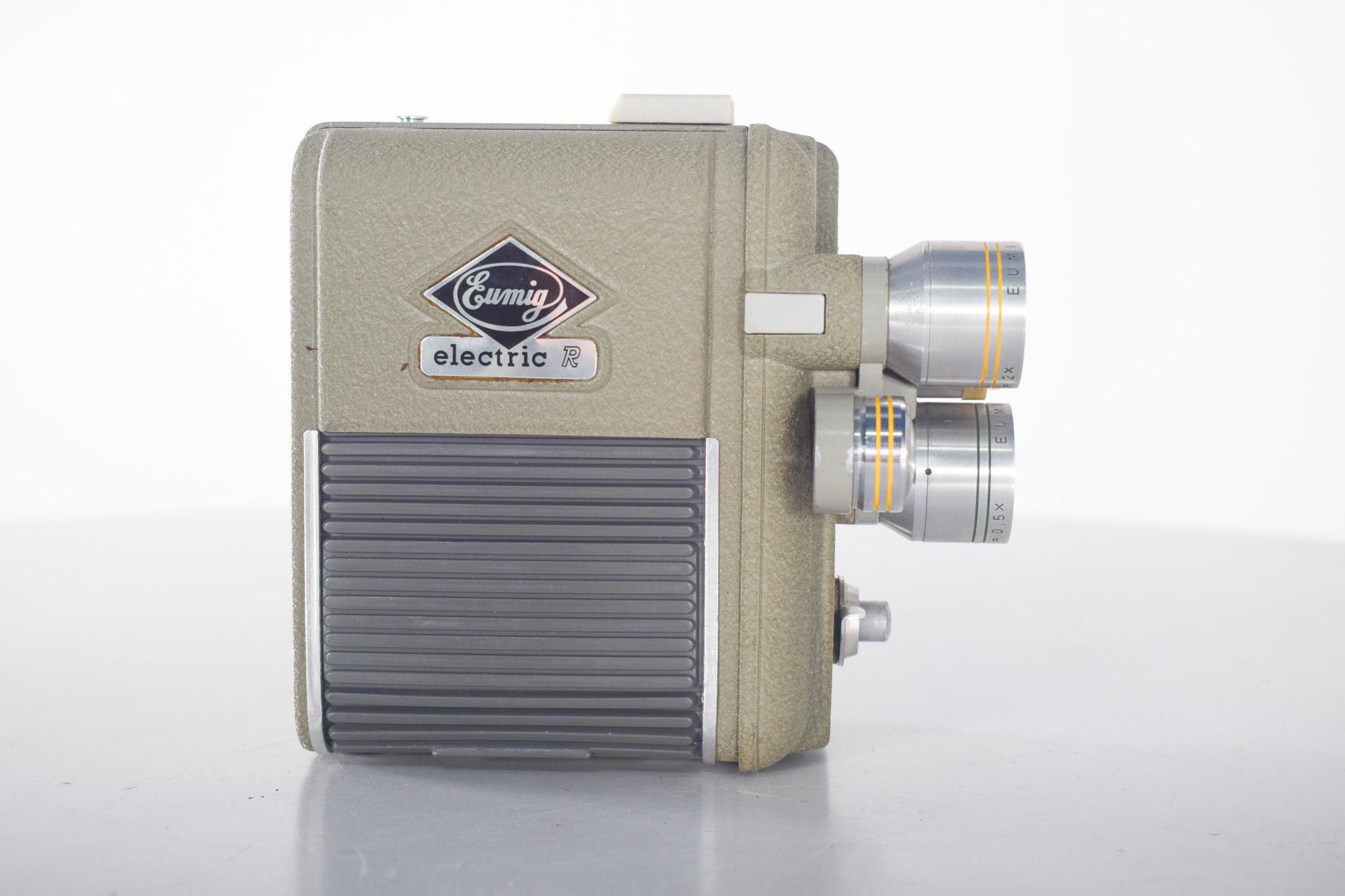 Eumig, Electric R, caméra vidéo 8 mm. Doté d'un étui en cuir, robuste et compact, cet appareil photo 8 mm se distingue par son boîtier métallique texturé dans un ton beige verdâtre et ses trois objectifs rotatifs, qui permettent de sélectionner
