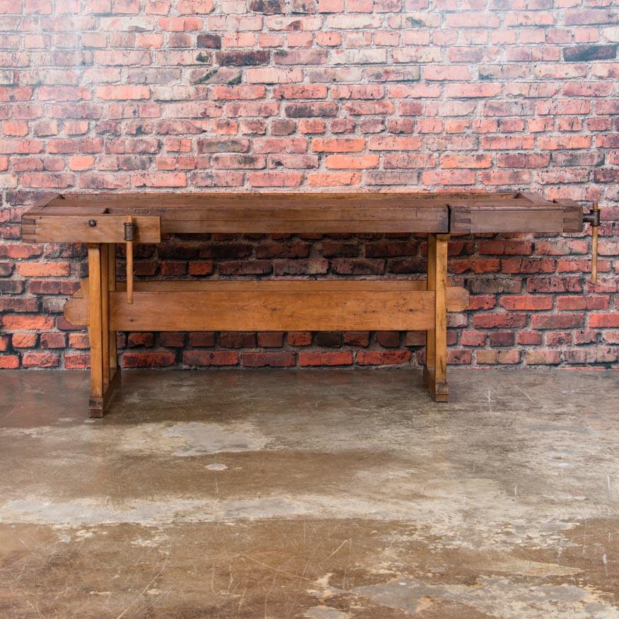 The character and appeal of this workbench come from the aged patina that can only develop over decades of use. There is a pair of vices, one on each end, with a wood handle and recessed tray where the carpenter would lay his tools and for catching