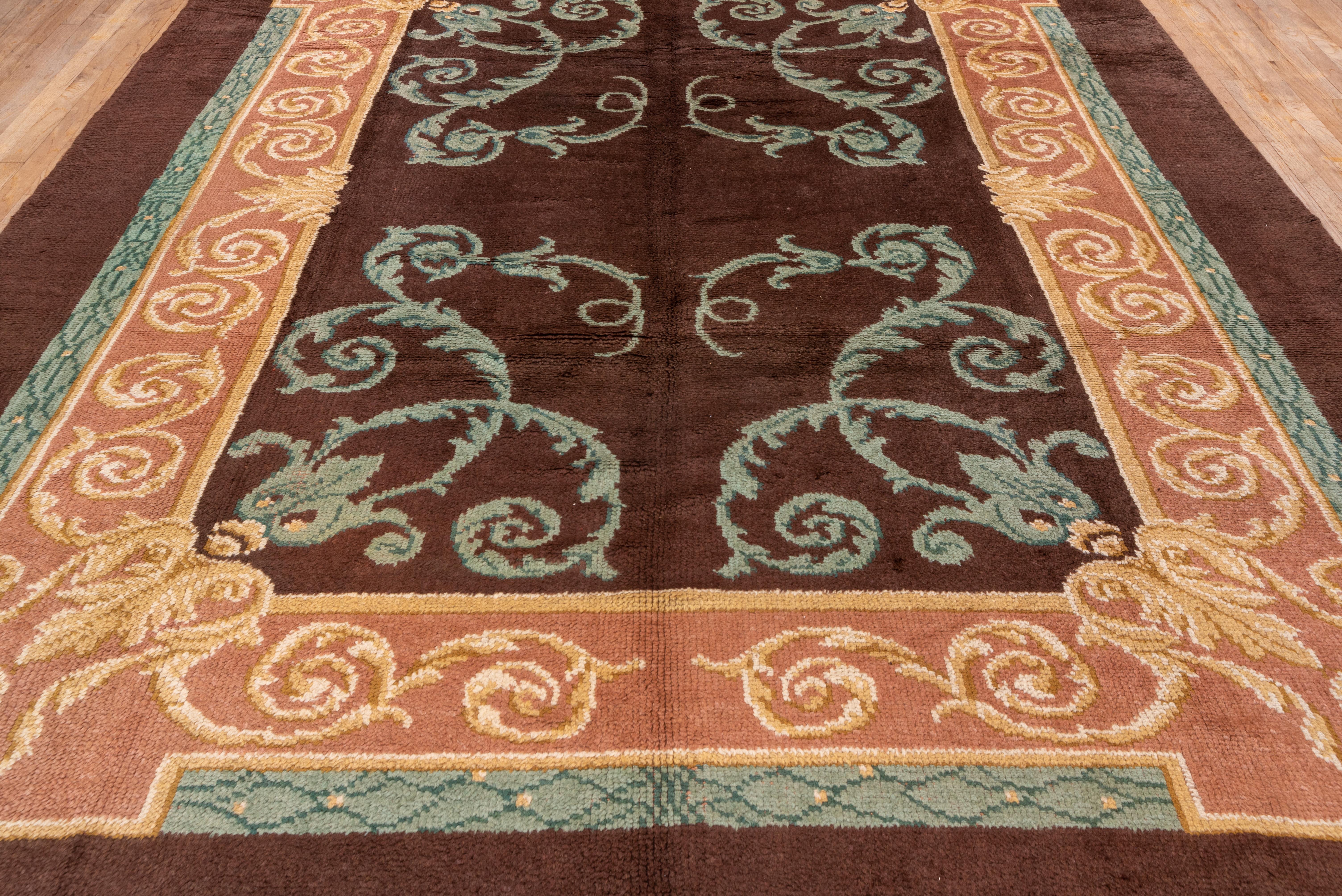 This coarsely knotted carpet with glossy wool has a simple large spiral acanthus design in teal n the warm brown ground. The main salmon-brown border shows more acanthus volutes, within a wide sienna brown plain outer surround. The style is