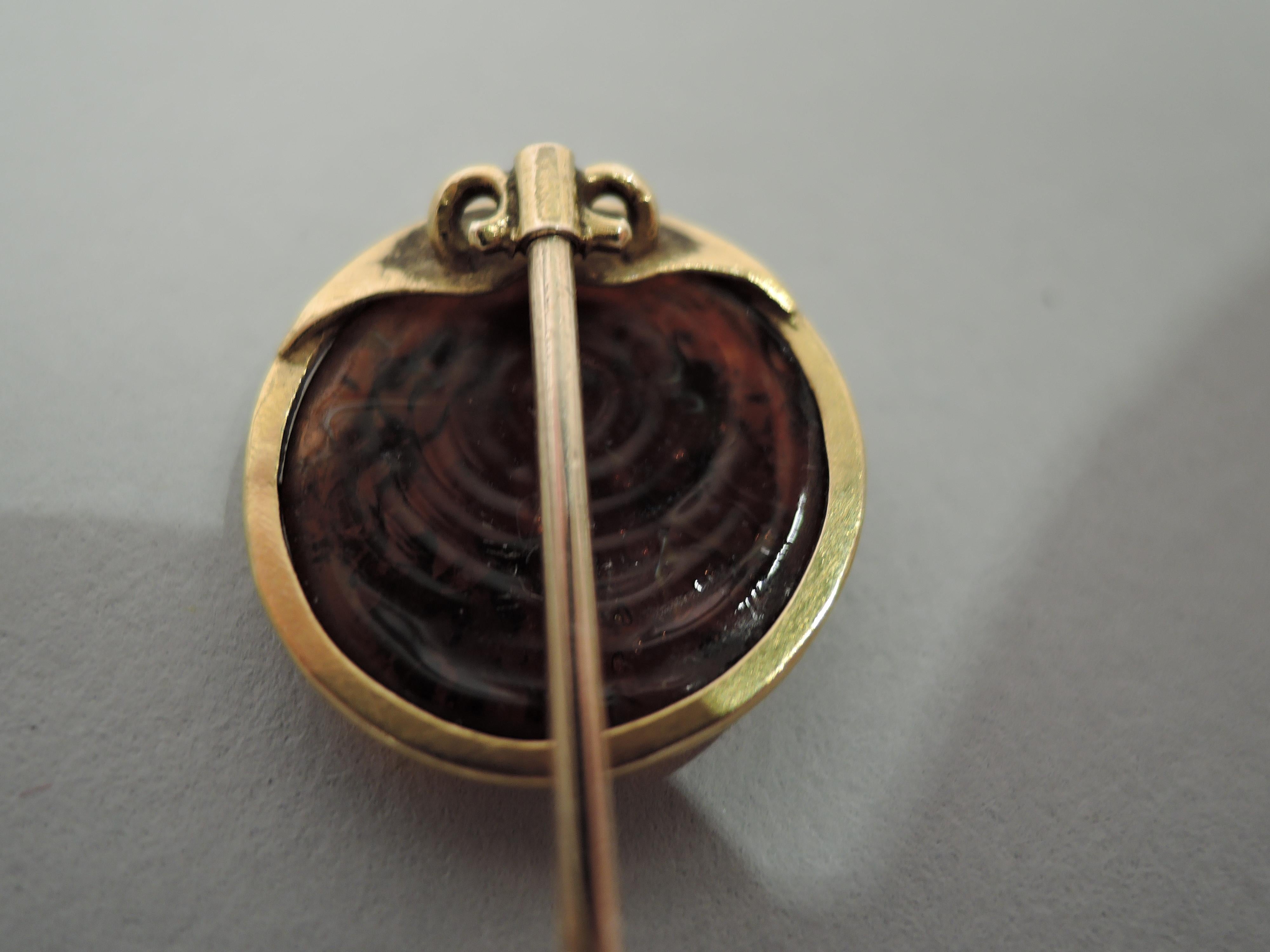Europäische Anstecknadel aus 15-karätigem Gold mit geschnitzter Intaglio-Kamee, die einen nach links gerichteten klassischen Frauenkopf darstellt. Die Farbe ist rötlich-braun. Sie befindet sich in einem goldenen Rahmen, der an einem gedrehten Schaft