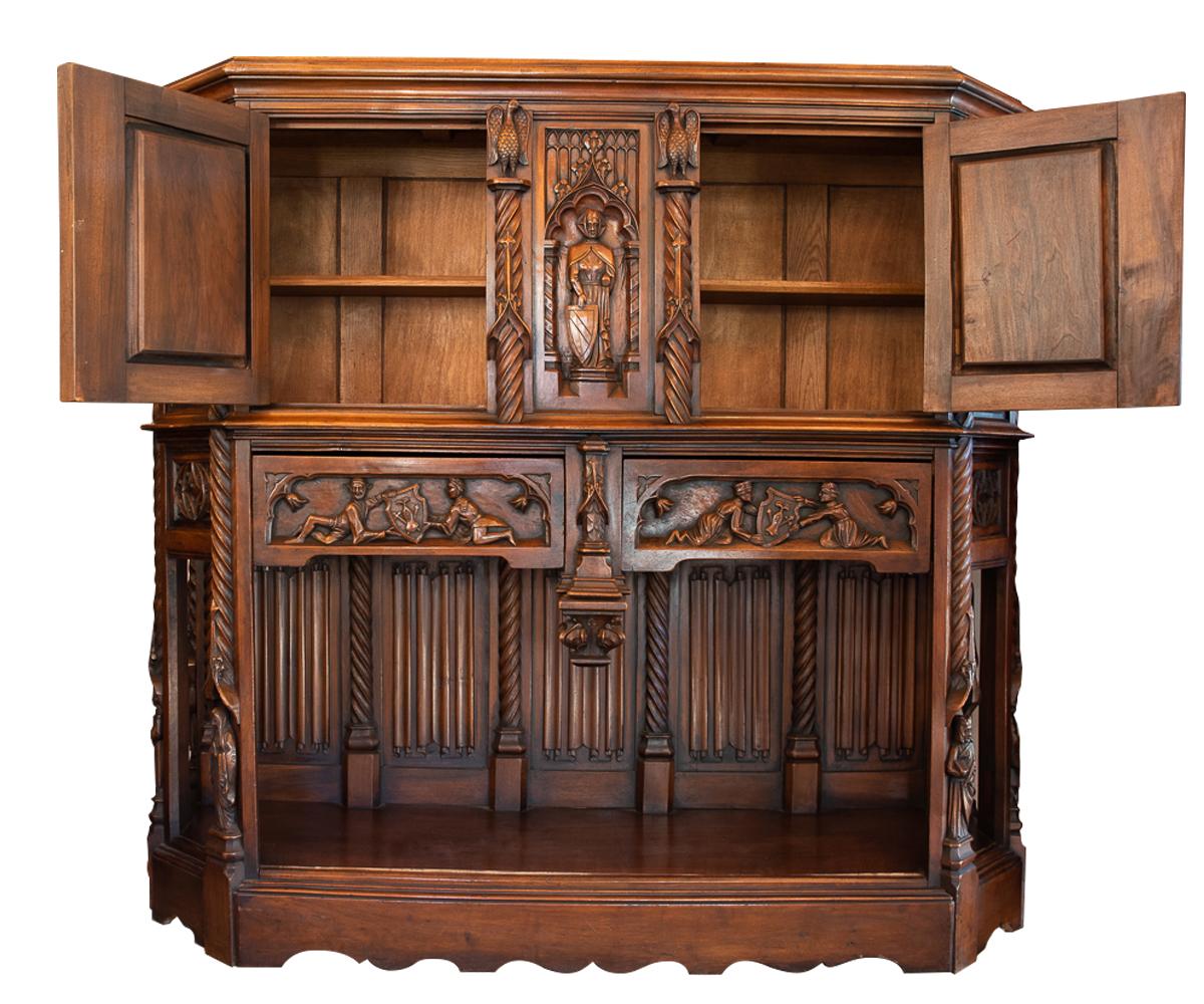 Offered is this antique hand carved walnut gothic style cabinet with linen fold panels. This cabinet has a lion holding a family crest, knights riding on horses, jester, nuns and an eagle so it covers most of the familiar gothic subjects. It is a