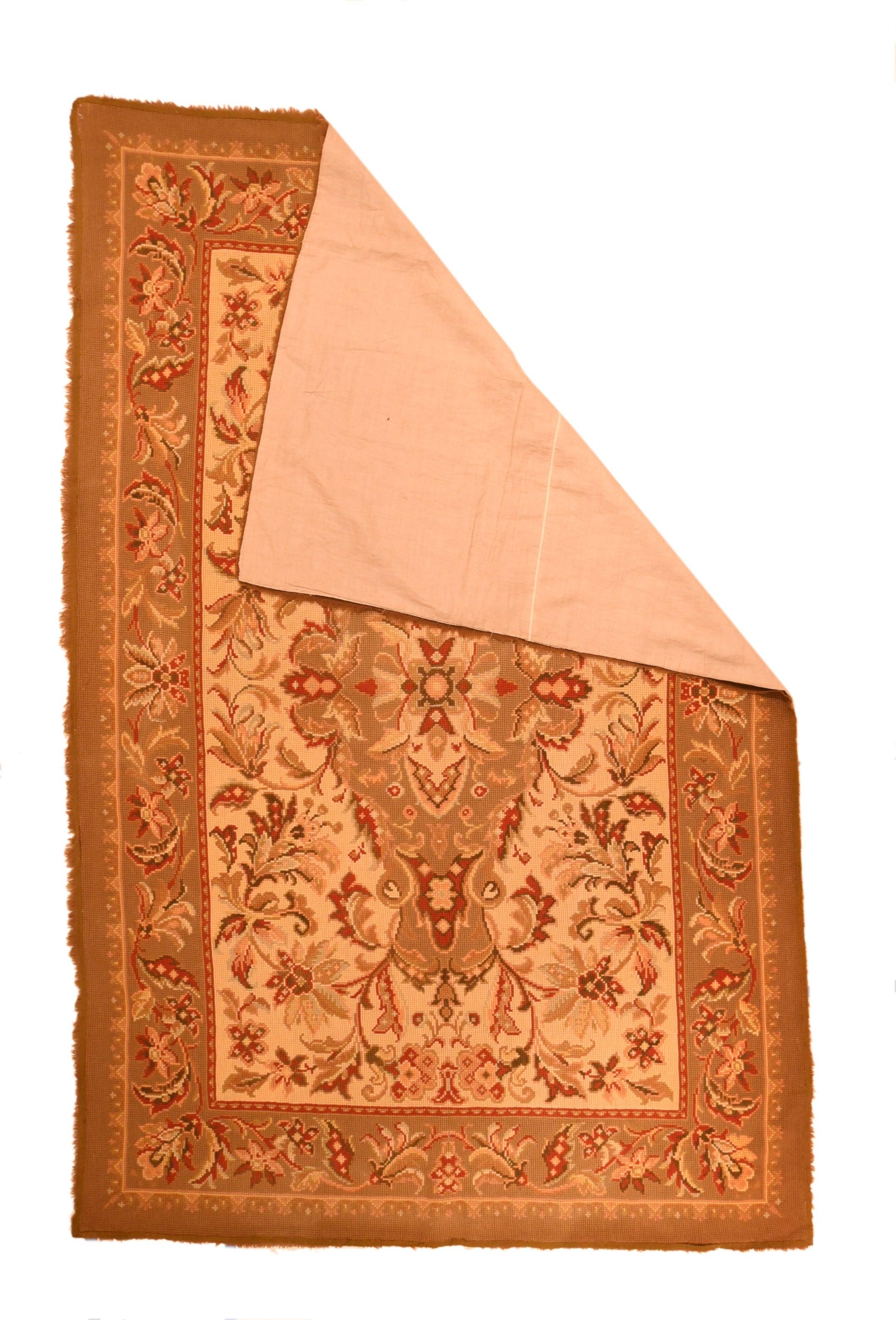 Tapis européen antique à aiguilles 4'9'' x 7'6''. Dans un style urbain tout à fait persan, avec un champ crème paille présentant un grand médaillon aux tiges courbes et feuillues, et enfermant des feuilles et des fleurons. Les fleurs des champs ont