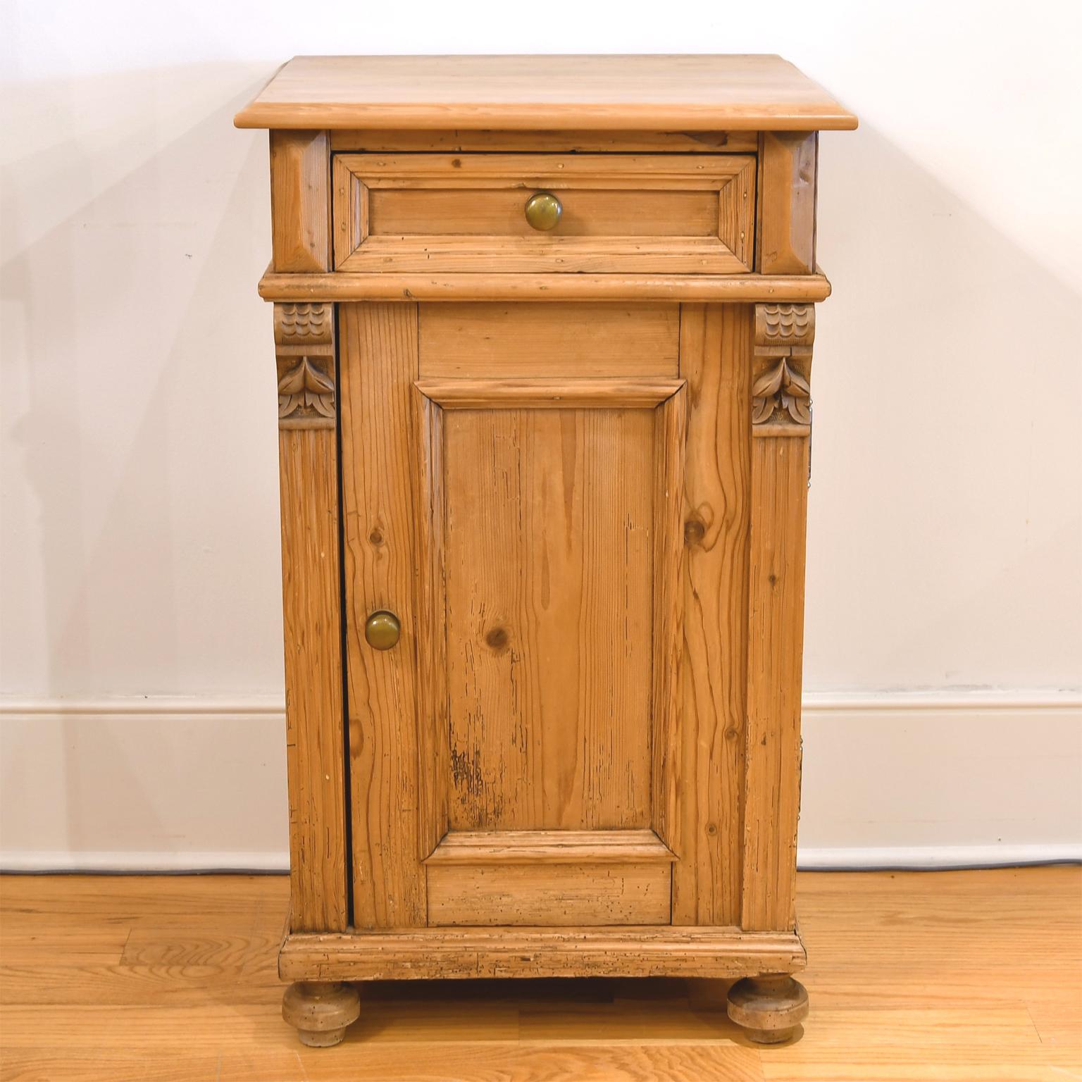 Austro-Hungarian pot cupboard or nightstand in scrubbed & waxed European pine offering a paneled drawer above a paneled cabinet with fluted pilasters on the sides & carved decorative escutcheons. Cabinet comes with brass pulls, interior shelving &