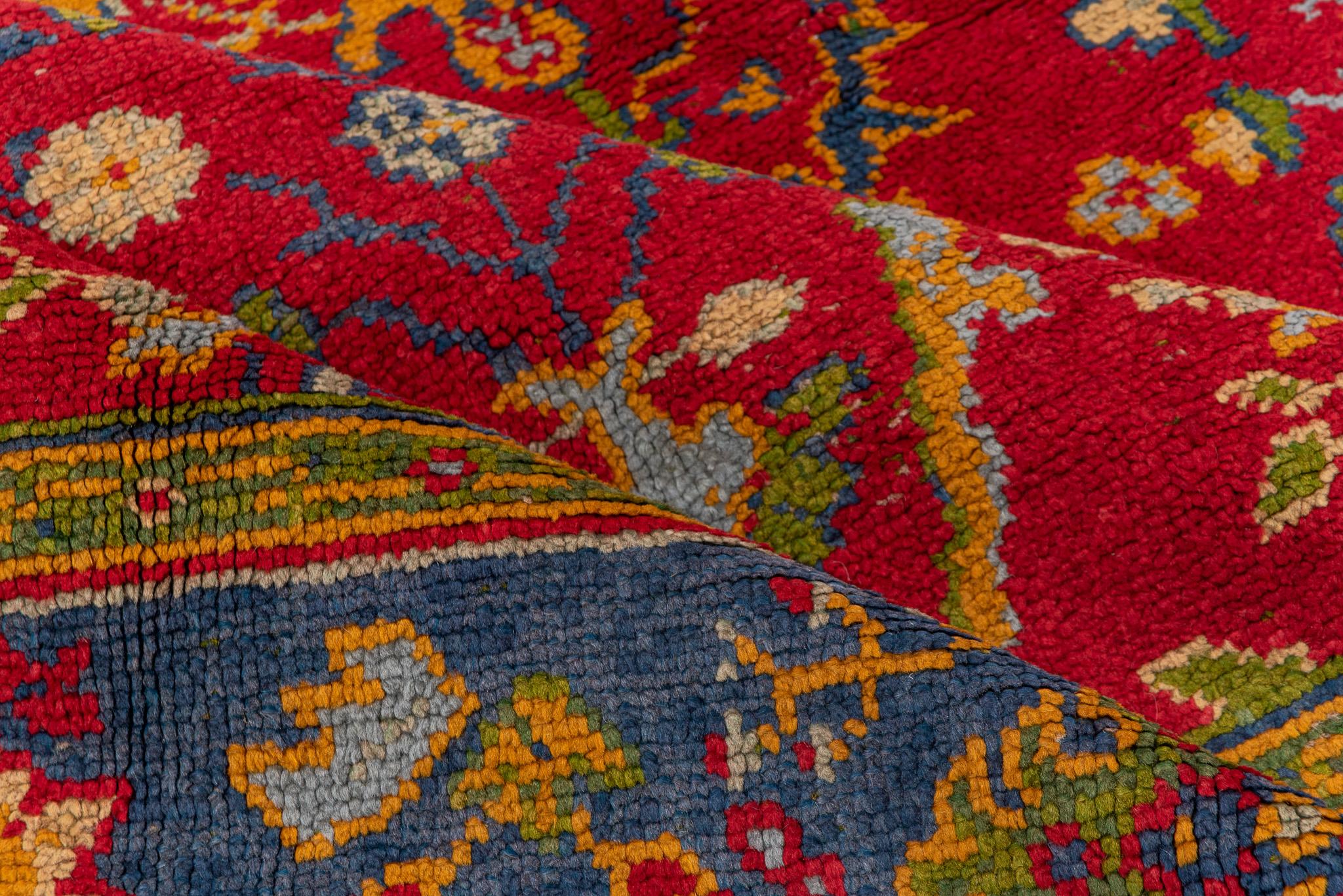 Esta vibrante alfombra de estilo europeo, que mide 7,2 x 10,5, irradia colores vivos e intrincados diseños florales. El profundo campo carmesí está adornado con una serie de rombos simétricos, cada uno de ellos lleno de exuberantes motivos botánicos