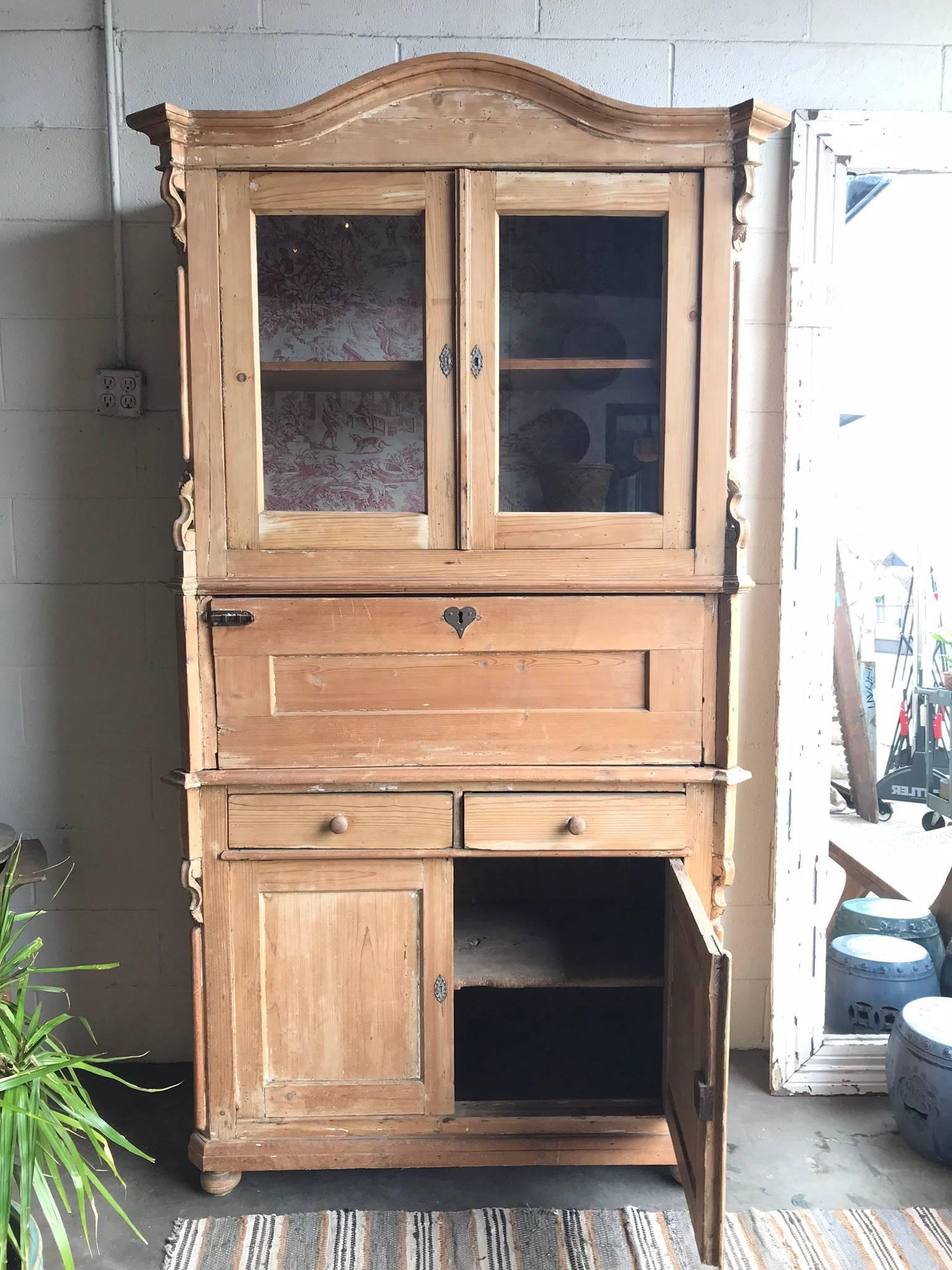 Early 1900s European pinewood hutch. Featuring beautiful antique hardware, glass cabinet doors, carved wooden moulding, and lined interior. This is a three-piece hutch with working drawers and a drop-down writing surface.

- drop-down desk height: