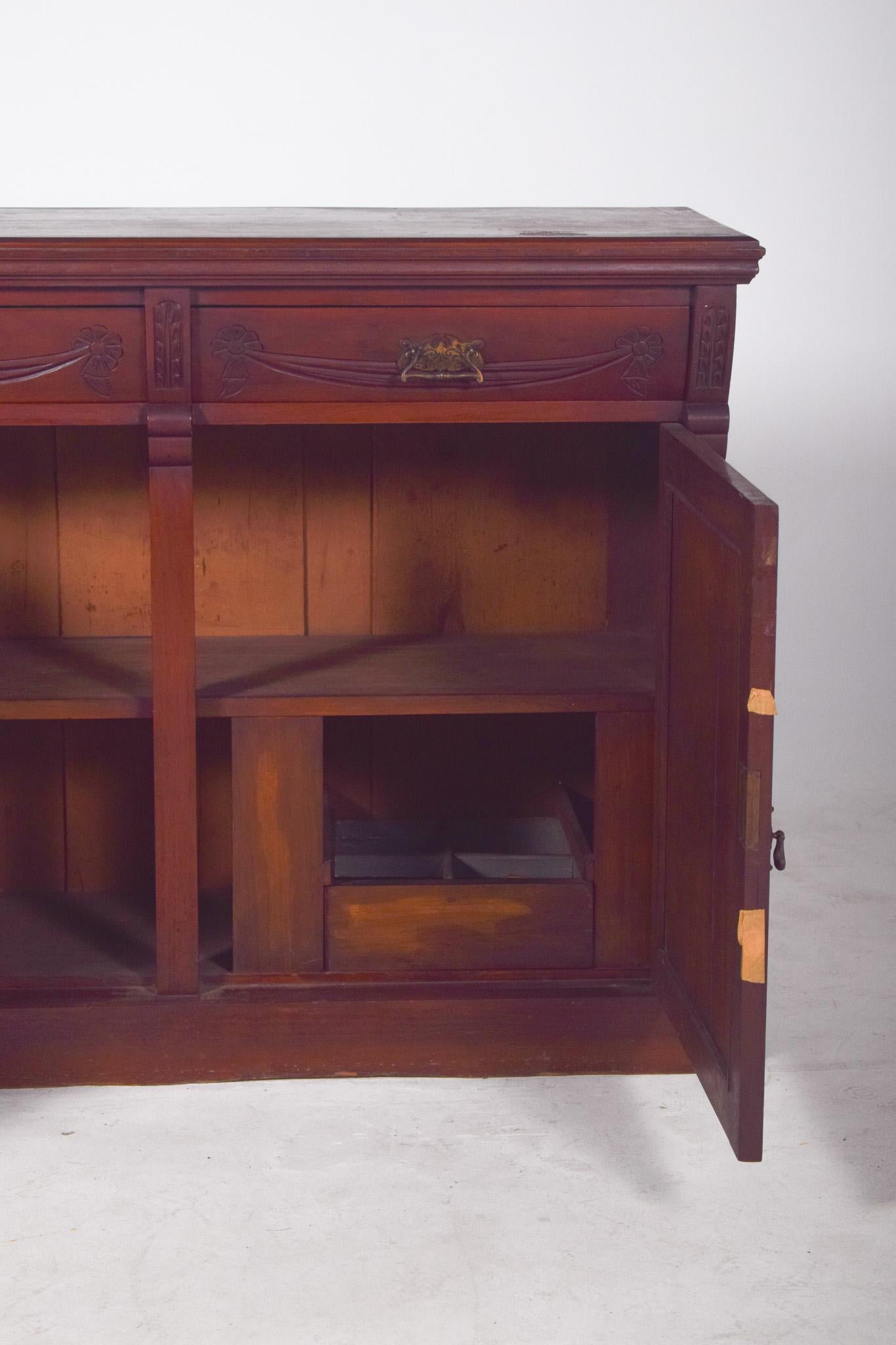 Sideboard with two different doors. In dark wood with richly detailed carvings on the front doors. Two large lower doors stand out, decorated with bas-reliefs framed by geometric shapes and central shields with floral motifs and foliage. The
