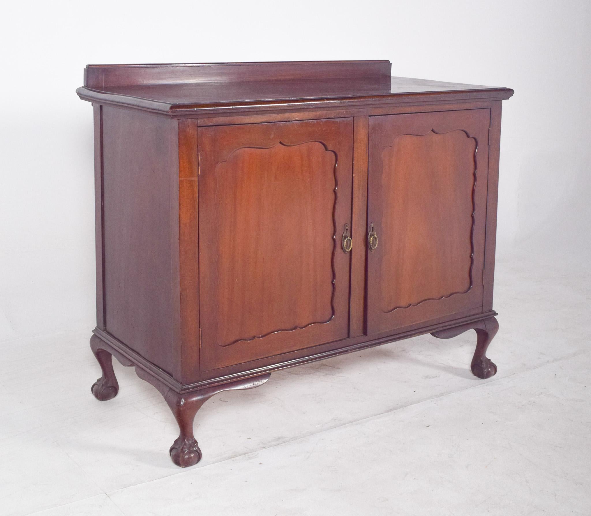 Two-door sideboard with a slight elevation. With a compact structure and balanced proportions, the doors are decorated with carved frames with a wavy cutout, creating a panel effect with slight relief and organic contours. The metal handles are