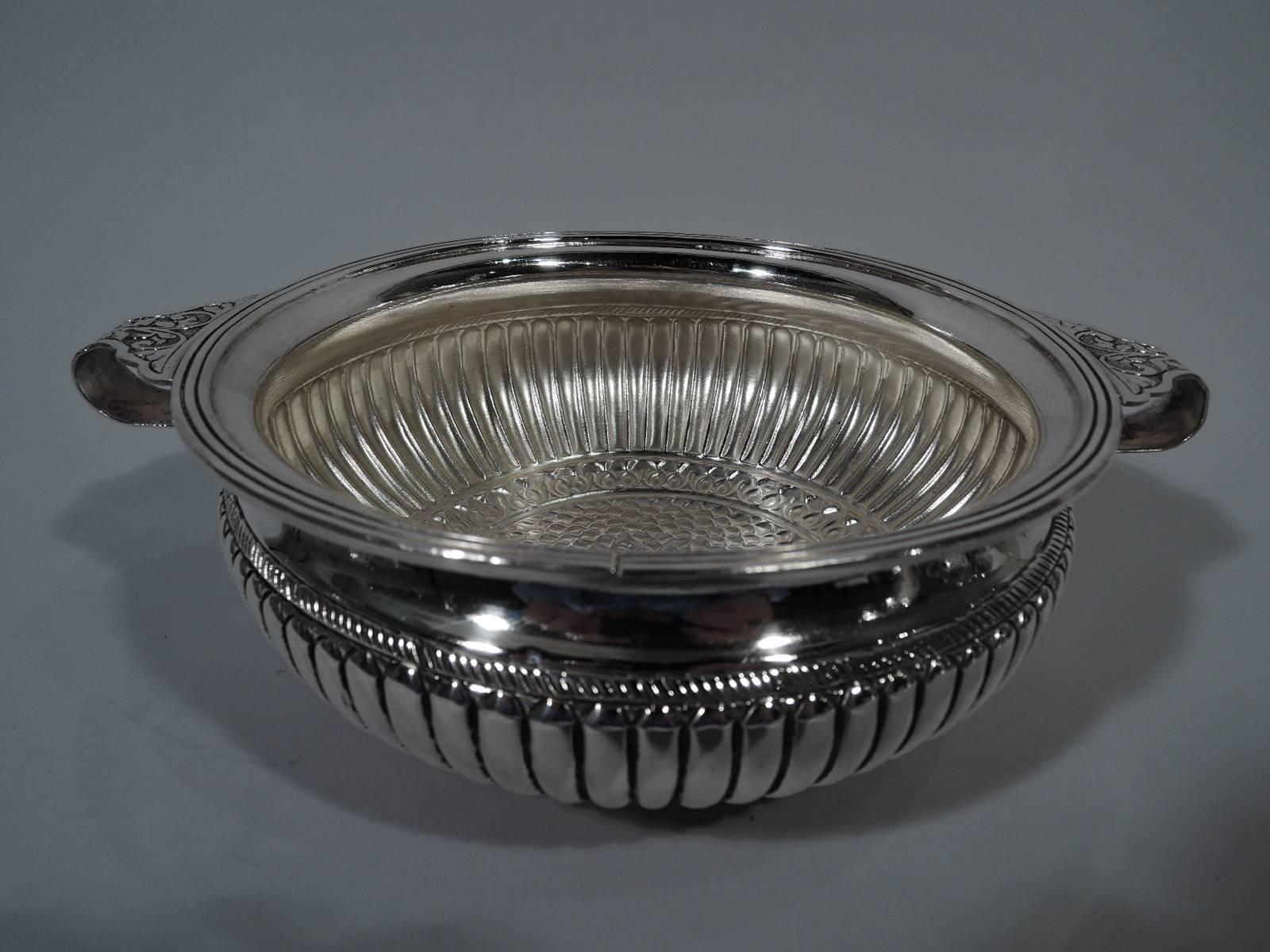 Antique European 800 silver bowl. Bellied with reeded rim and three round supports. Side handles have scalloped mounts with leaves and scrolls on stippled ground. On exterior the sides are gadrooned and the bottom has central flower surrounded by