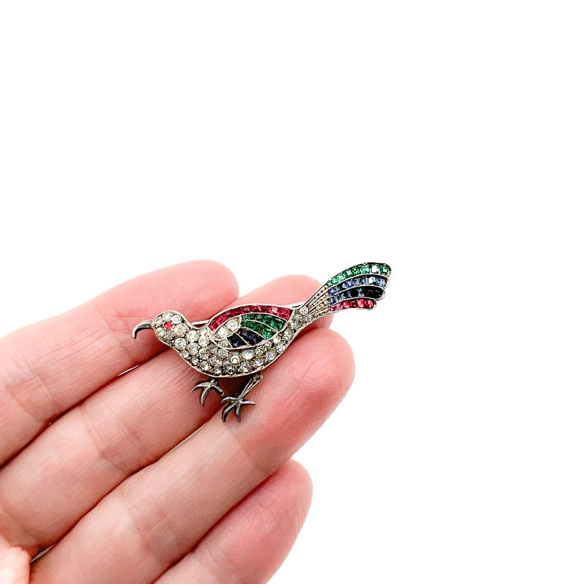 An antique exotic bird brooch from the 1920s. Exquisite attention to detail and craftmanship sets this piece apart as a miniature piece of wearable art from a century ago. Crafted in sterling silver and set with paste stones. The coloured glass