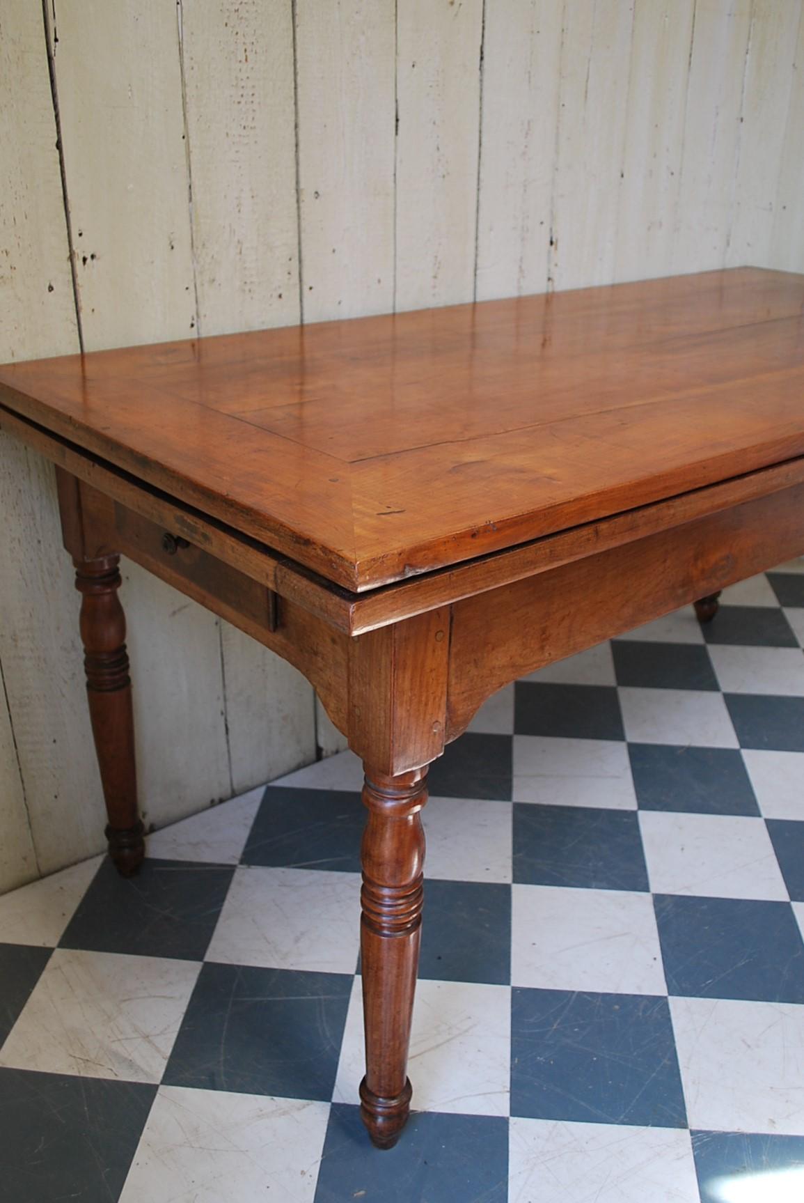 A very good quality early 19th century French cherrywood farmhouse table with extending ends. Beautifully patinated and figured top with a framed border, standing on well proportioned turned legs. The original shaped frieze incorporates a cutlery
