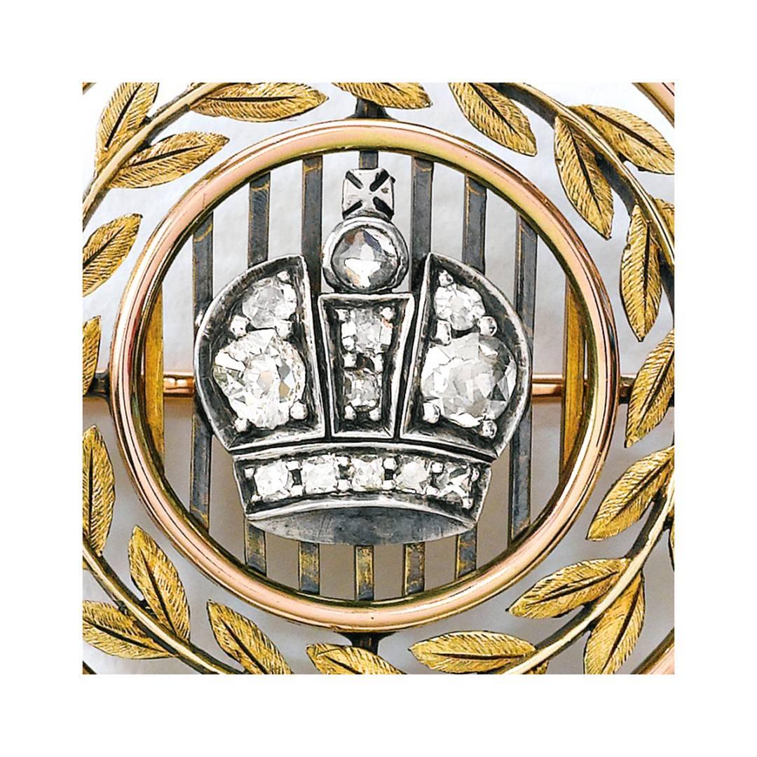 A Fabergé Imperial Presentation diamond-set vari-color gold brooch, workmaster Eduard Schramm, St. Petersburg, circa 1899-1904.  Circular in shape, the frame of the brooch in red gold, the grille-form centered with a diamond-set Imperial crown, the