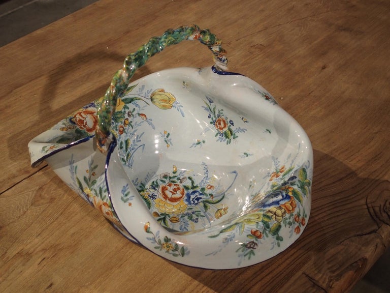 This is a charming antique French faience basket dating to circa 1900. It has a fantastic shape with its edges at either end folding over as it if were composed of a pliable material. The multicolored twisted rope handle holds up the center portion.