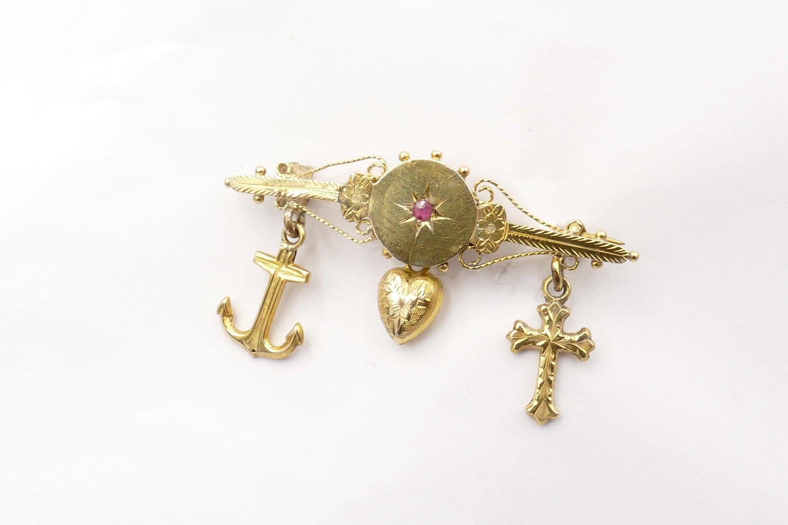 9ct Yellow Gold Victorian Brooch with the 3 hanging charms - an Anchor, a Heart & a Cross, 
depicting Faith Hope & Charity.
It features one reddish-purple Ruby in the centre of the Bar, eye clean & of medium tone.
The Brooch has Foliate detailand