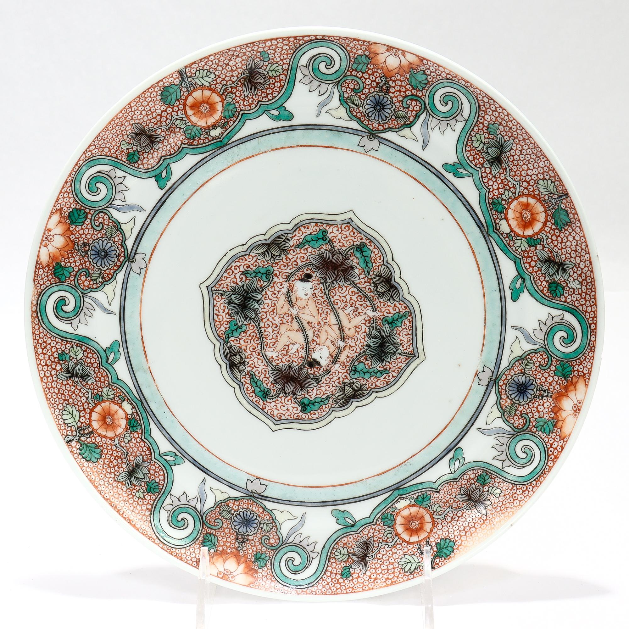 Ein feiner antiker chinesischer Export-Porzellanteller.

Dekoriert in einem famille verte Variante zentriert auf eine Kartusche mit Zentrum auf der He-He Er Xian (oder Hehe Zwillinge) unter den Lotusblumen. 

Die Hehe-Zwillinge sind