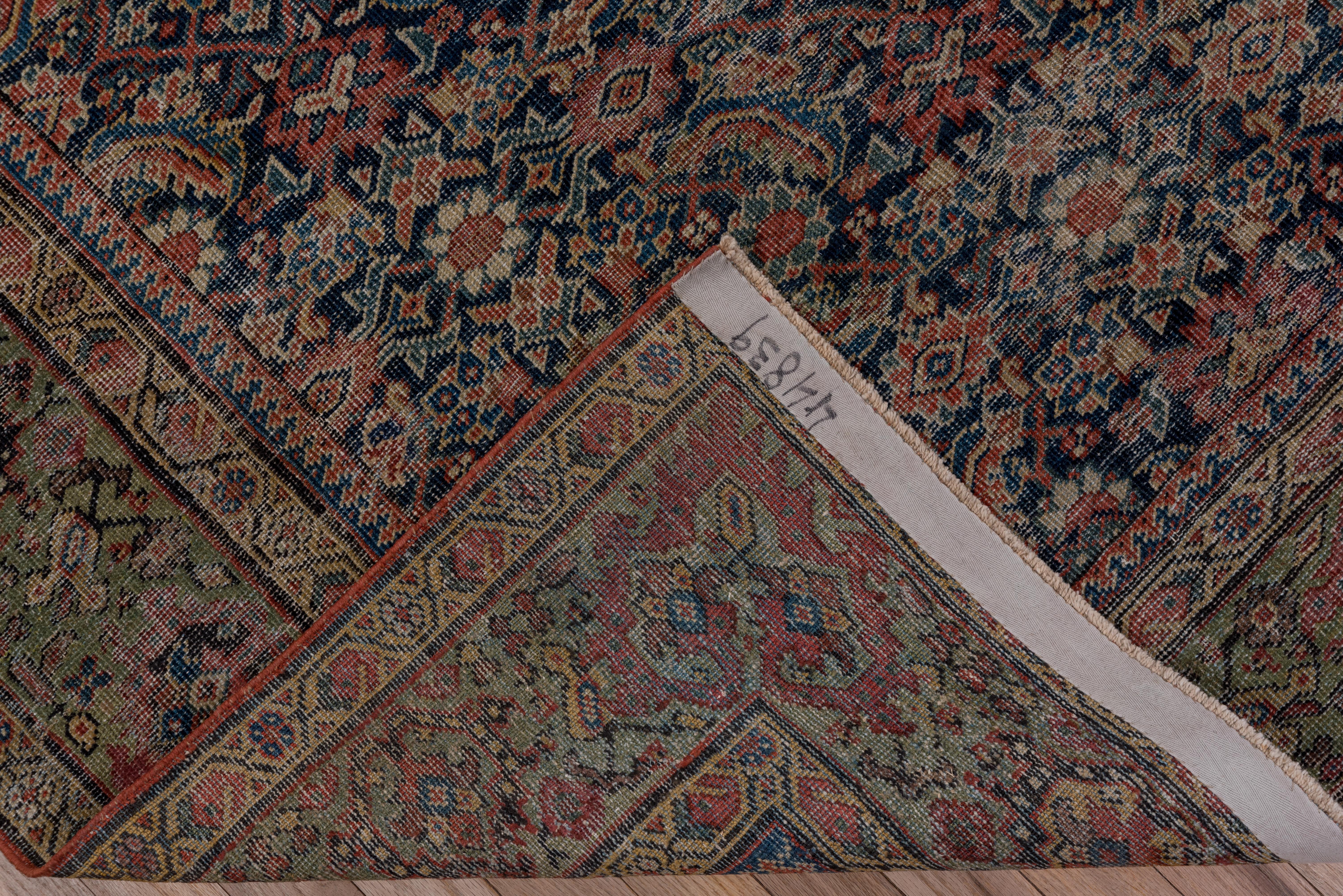 Ce tapis rustique de taille galerie, de style classique persan occidental, présente un dense motif Herati sur toute sa surface, avec des fleurs ivoires, des palmettes vertes et des feuilles de 