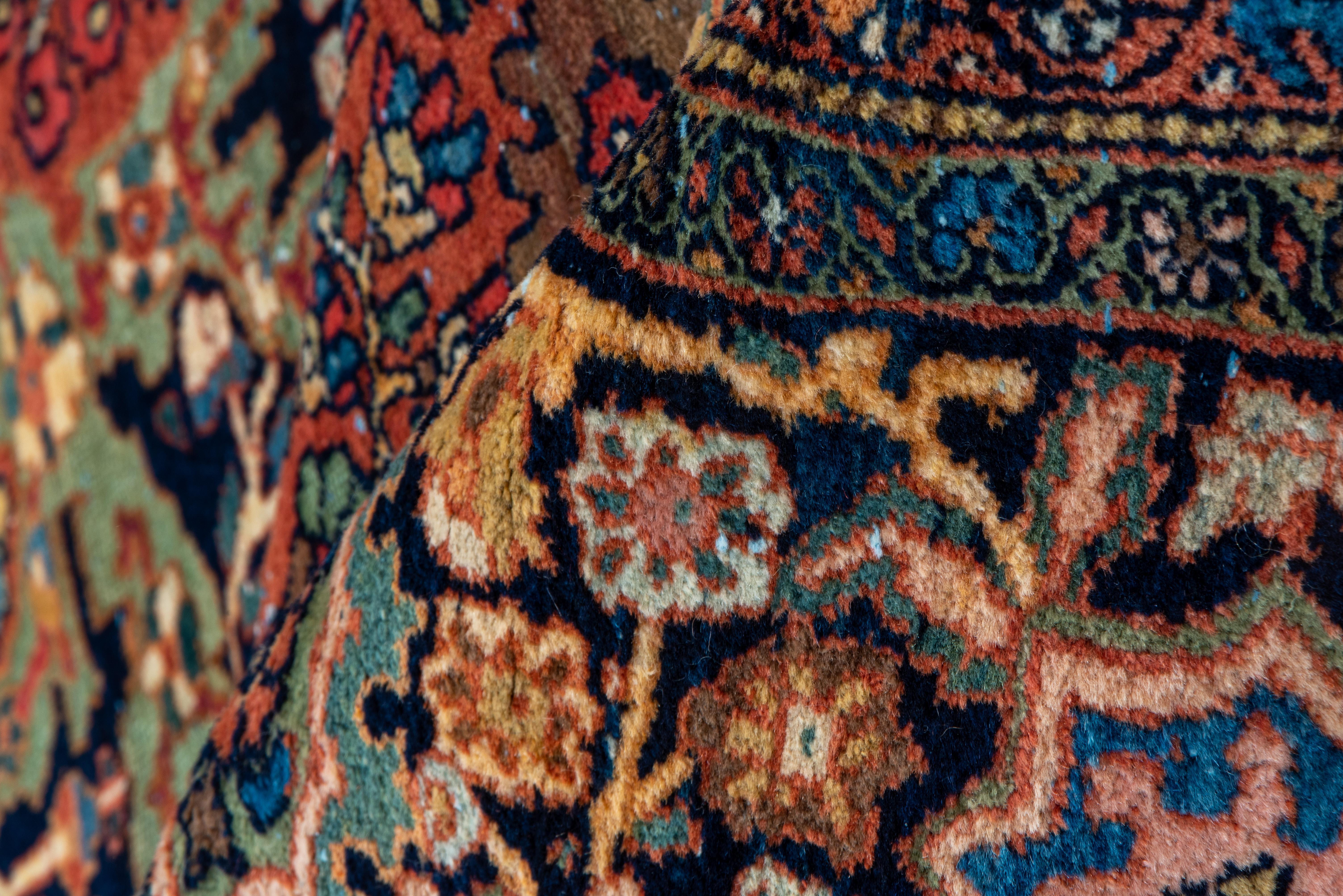 Dies ist ein klassischer westpersischer Dorfteppich im urbanen Stil mit einem mit Blumen und Arabesken gefüllten rostfarbenen Feld, einem navyfarbenen Medaillon mit kleinen Anhängern und navy- und elfenbeinfarbenen erweiterten Ecken. Marineblaue
