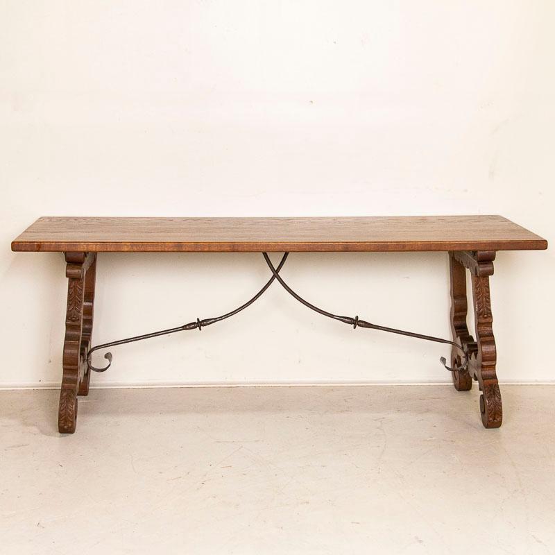 This fascinating 6.5' oak dining table holds visual intrigue due to the unique Spanish style base. Notice the carved scalloped and curved details of the harp/lyre shaped legs that are supported by a curving double hand-forged iron stretcher. Please