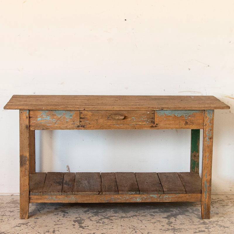 There is a worn and wonderful appeal to this old work table, due to the years of use reflected in it. Note the remains of old green and even blue paint that add to its vintage character as well. The single drawer and lower shelf make it ideal as a