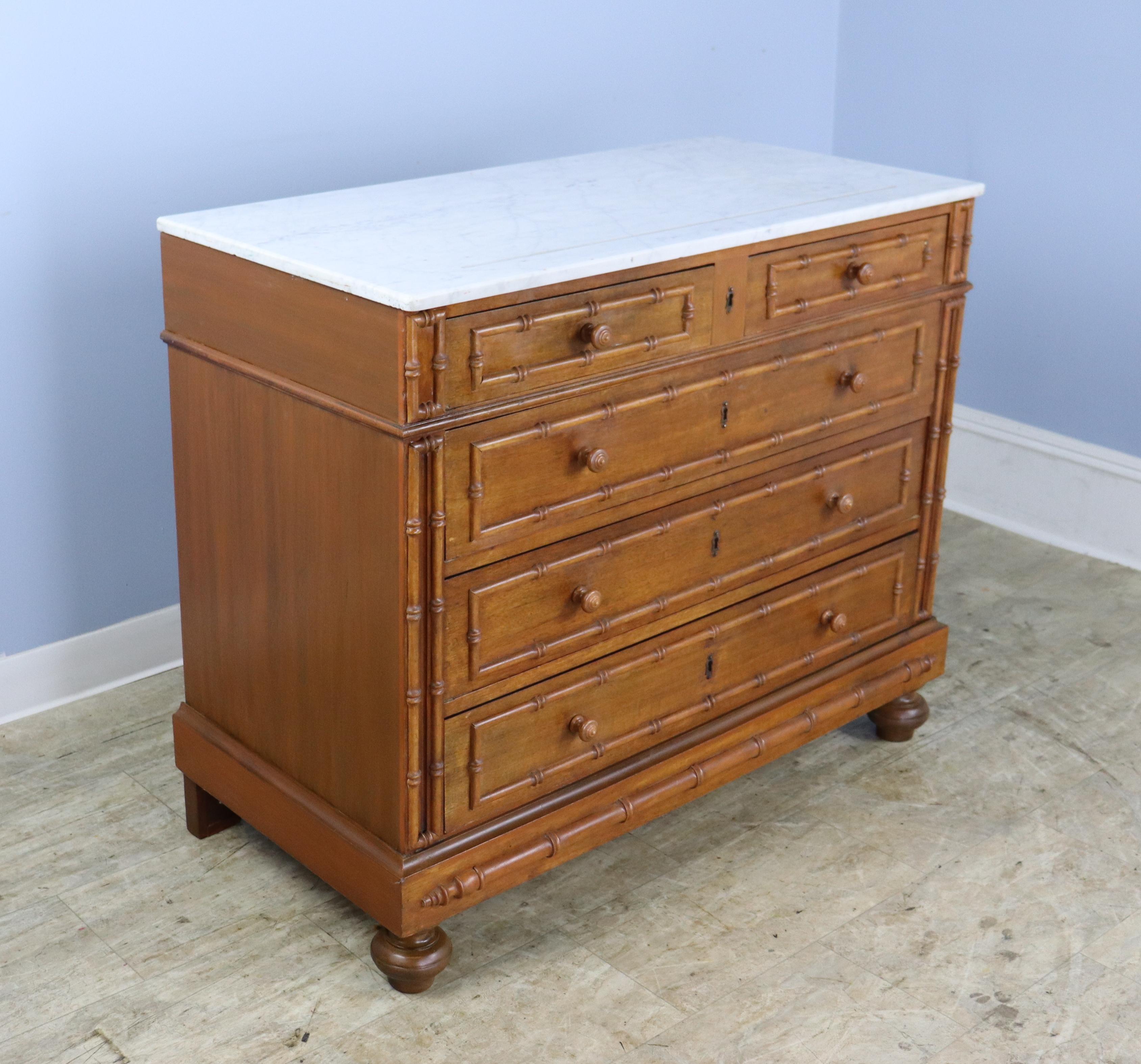 A charming chest of drawers with faux bamboo columns and mouldings. Two over three roomy drawers. The marble which is original is in good antique condition. There is smor light wear on the top of the marble, shown in thumbnail.
