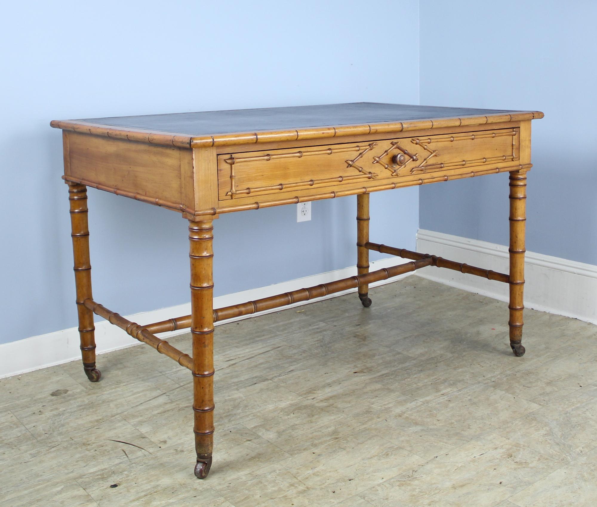 A wide and comfortable French faux bamboo desk with new dark brown leather top. Nice roomy drawer and attractive bamboo detail on the front. Castors are original and functional. 24 inch apron height is good for knees.