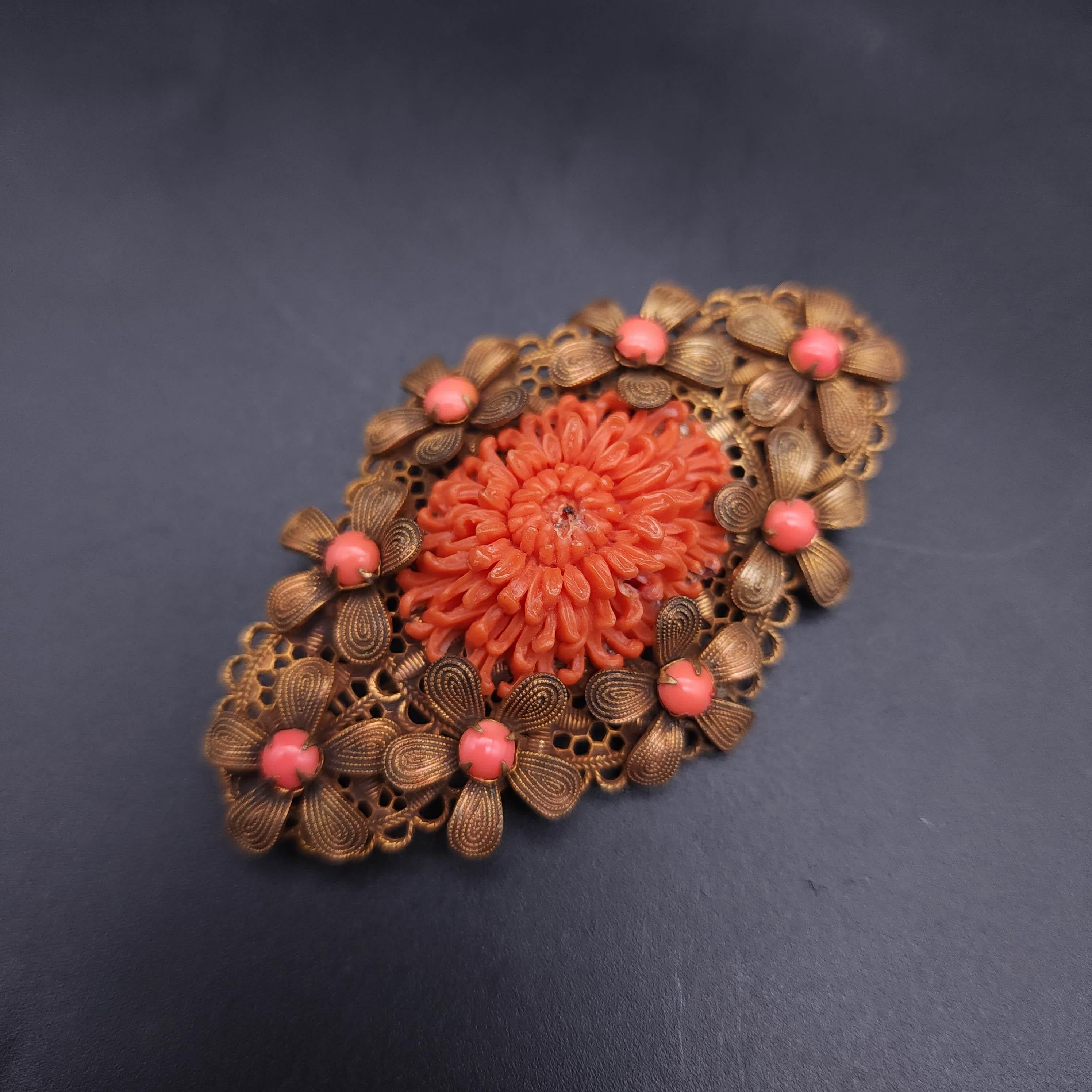 Discover the charm of vintage elegance with the antique floral brass pin, featuring a beautifully carved faux coral flower centerpiece. This exquisite pin is a testament to classic craftsmanship, adorned with intricate flower accents encircling the