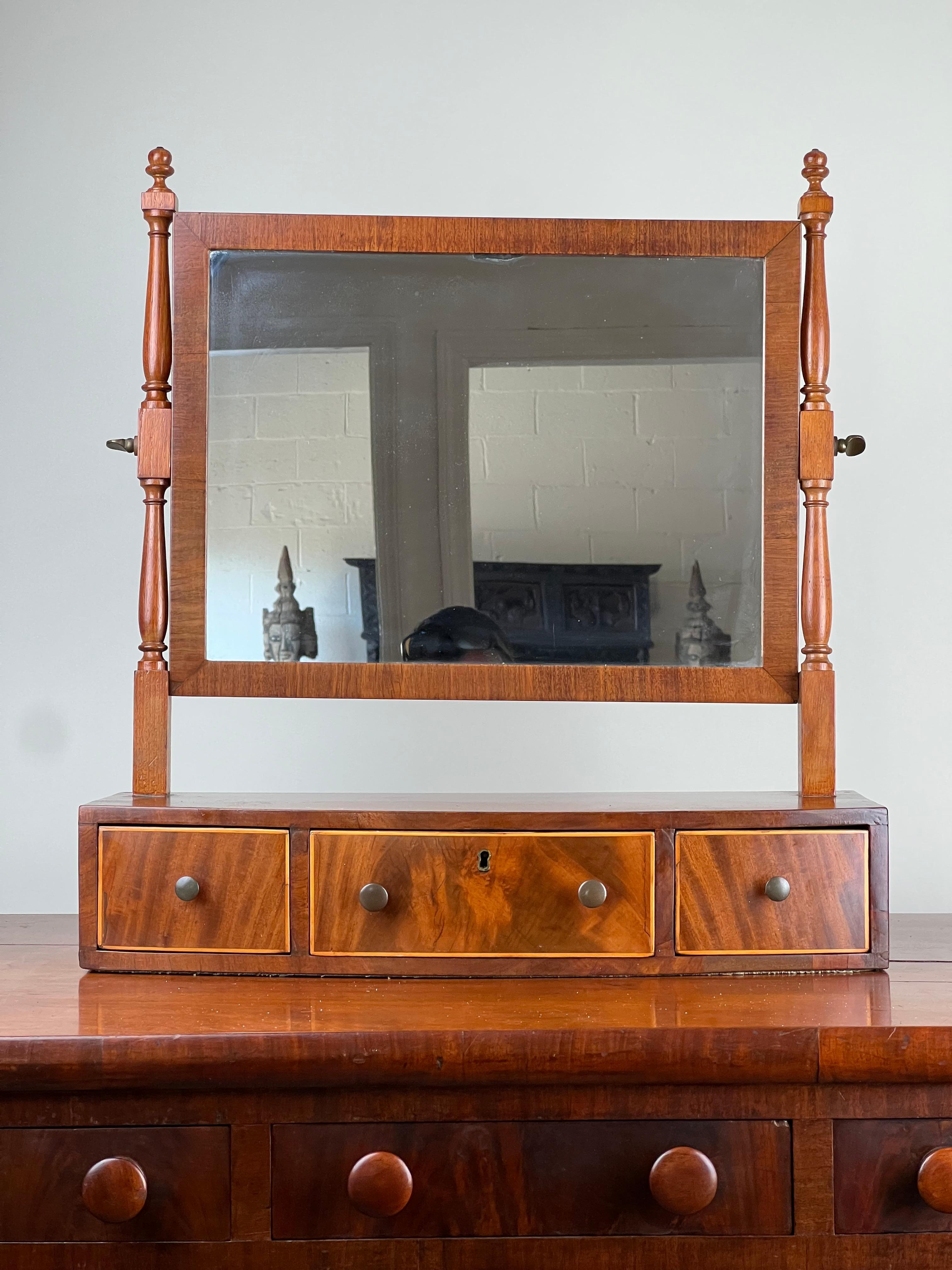 Cet élégant miroir de rasage en arc de cercle de la période Feder, datant d'environ 1830, est un bel exemple de l'artisanat américain du début du XIXe siècle. Fabriqué en acajou richement figuré, le miroir est encadré par des supports tournés avec