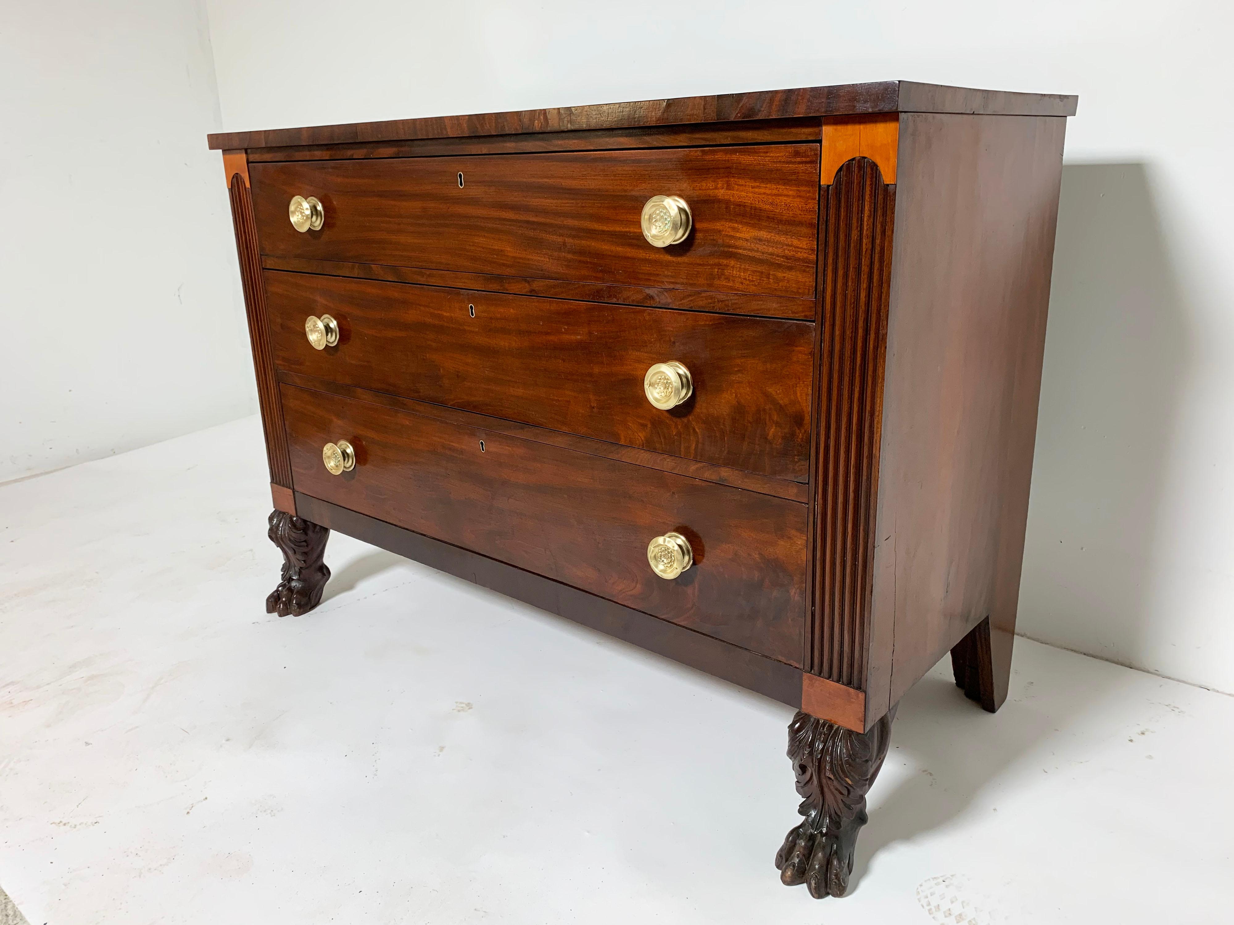 A Federal era three drawer chest in mahogany with hairy paw feet and spun brass pulls. The lighter maple patches above and below the reeded side panels arem a recognized feature of cabinet makers from the coastal Newport region.