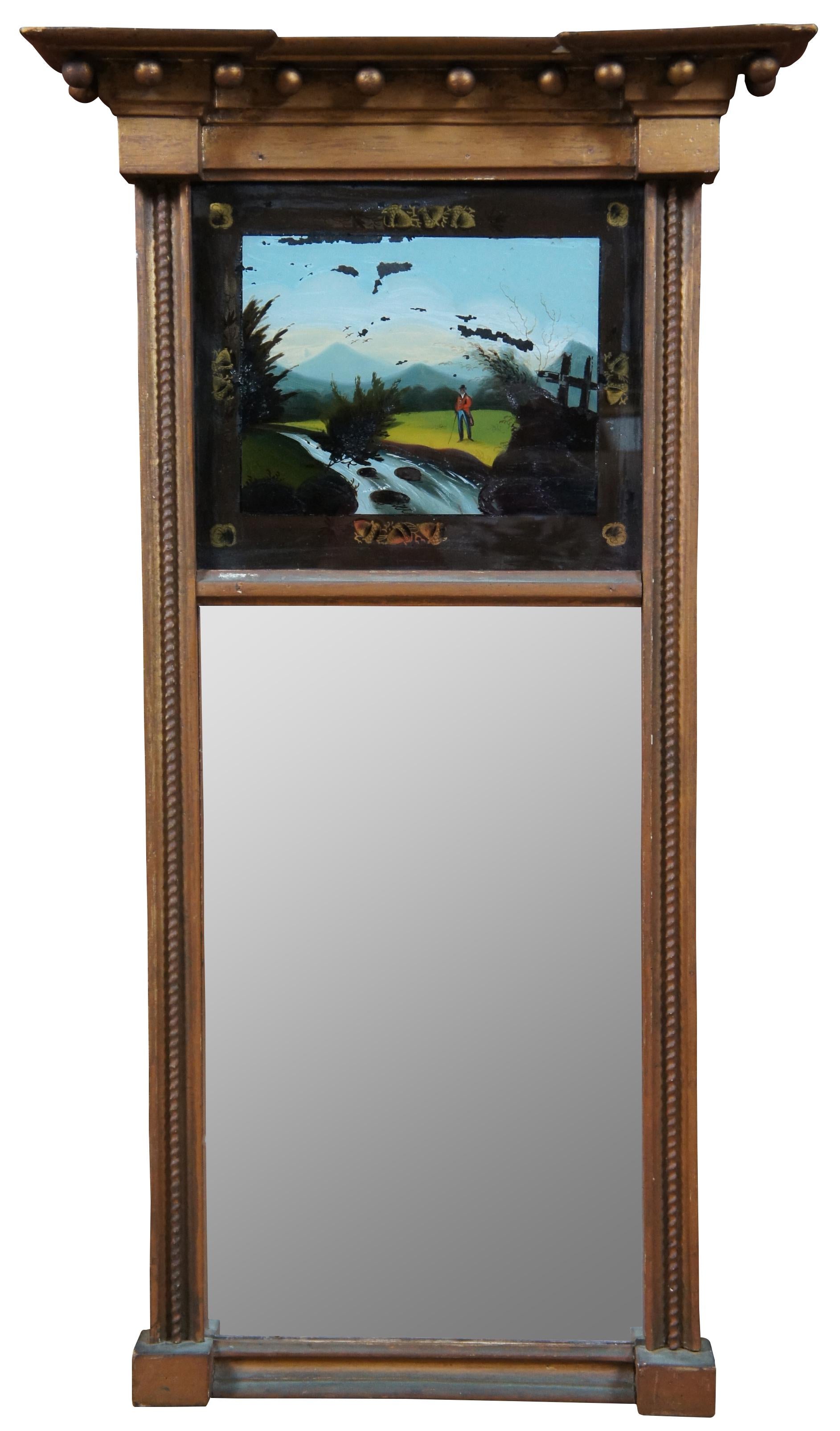 Early 19th century Federal period trumeau mirror. Features a giltwood frame with a reverse painted country landscape highlighted by a small river and a figure in a red jacket or tuxedo with a cane and top hat.

Measures: 17” x 3.75” x 30.5” /