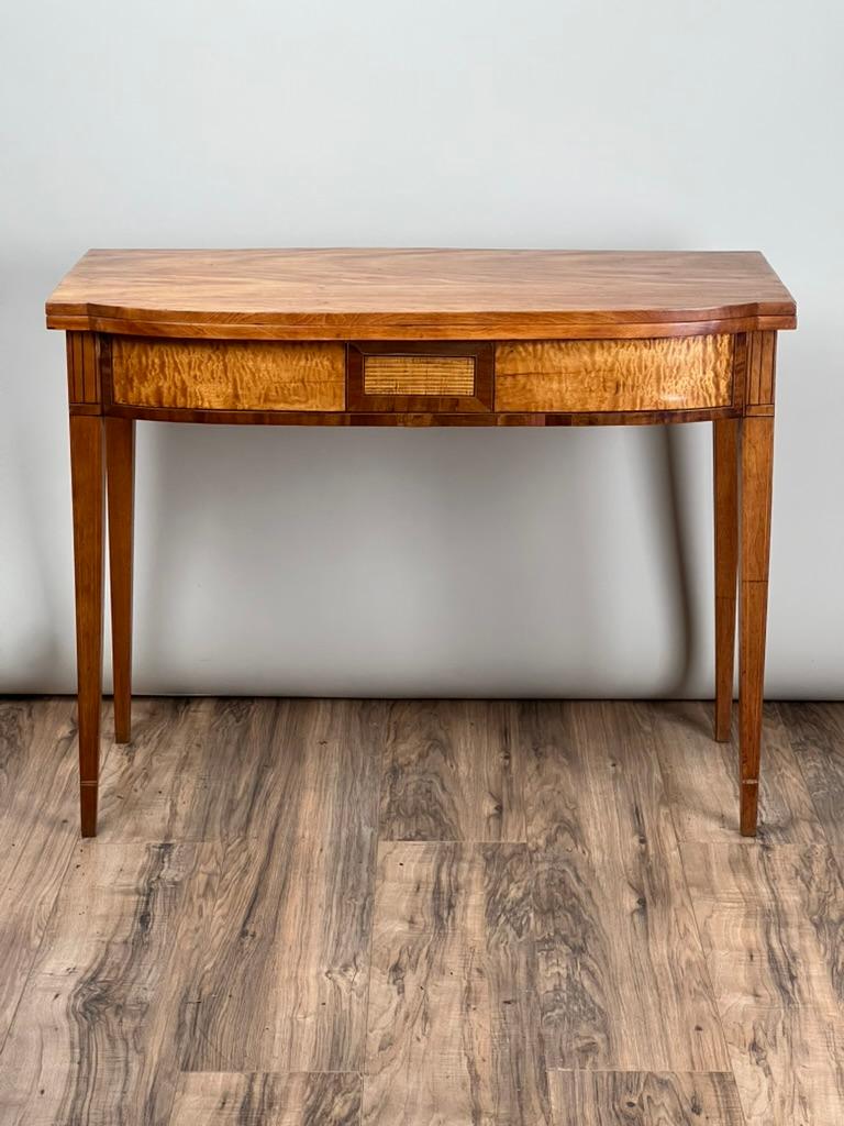Esta antigua mesa de juego federal Hepplewhite, de hacia 1830, presenta una llamativa fachada de arce tigre, famoso por su veteado vibrante y su calidad luminiscente, mientras que el resto de la mesa es de rica caoba, que ofrece un sutil contraste