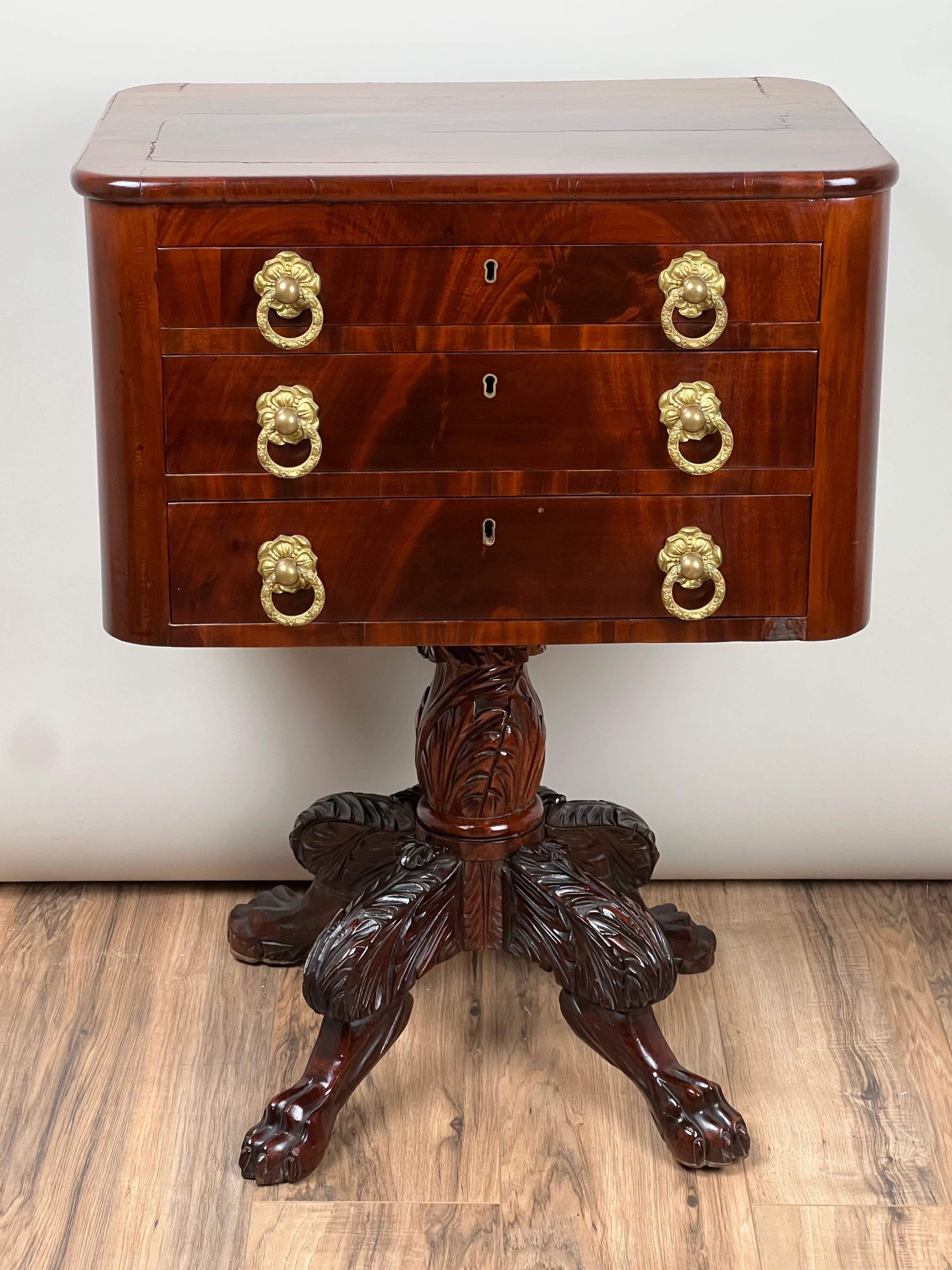 This Antique Federal Period Mahogany Three Drawer Stand, dating to around 1820, exemplifies the refined elegance of Federal-period design. Crafted from rich mahogany, the piece displays the wood’s deep, warm tones, enhanced by a subtle sheen that