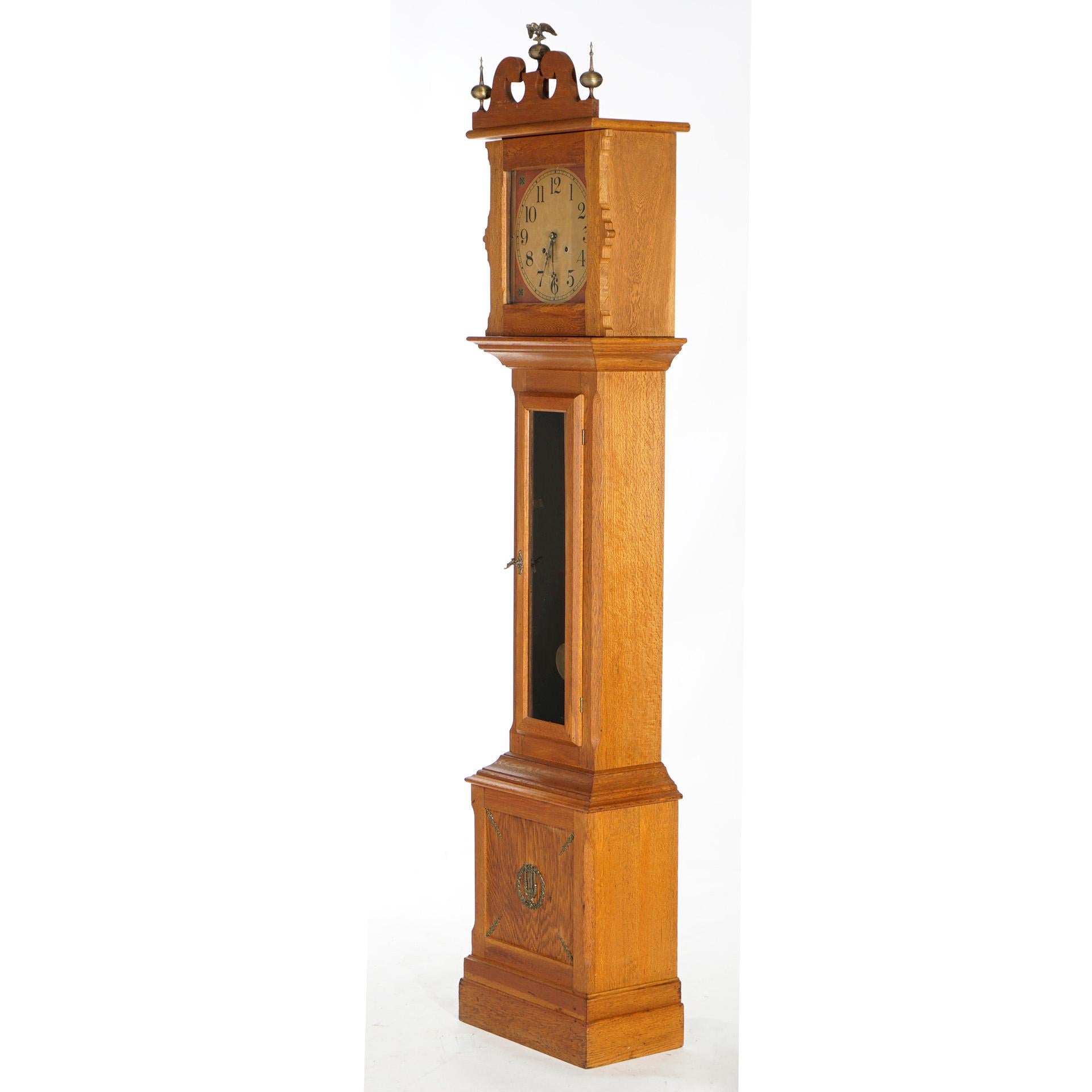Une horloge ancienne de style fédéral à haut boîtier par Ithaca offre un boîtier en chêne avec un capot en arc brisé avec un aigle central et des fleurons en forme de boule et de flèche, une colonne avec une porte vitrée sur la base avec des